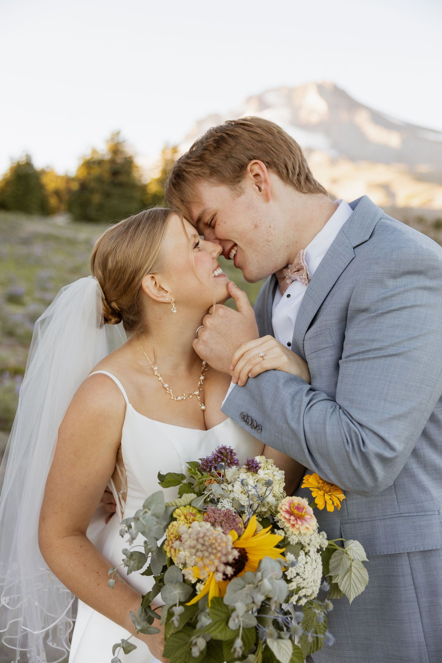 Intimate wedding portrait against mountain backdrop with sunflowers and wildflower bouquet.