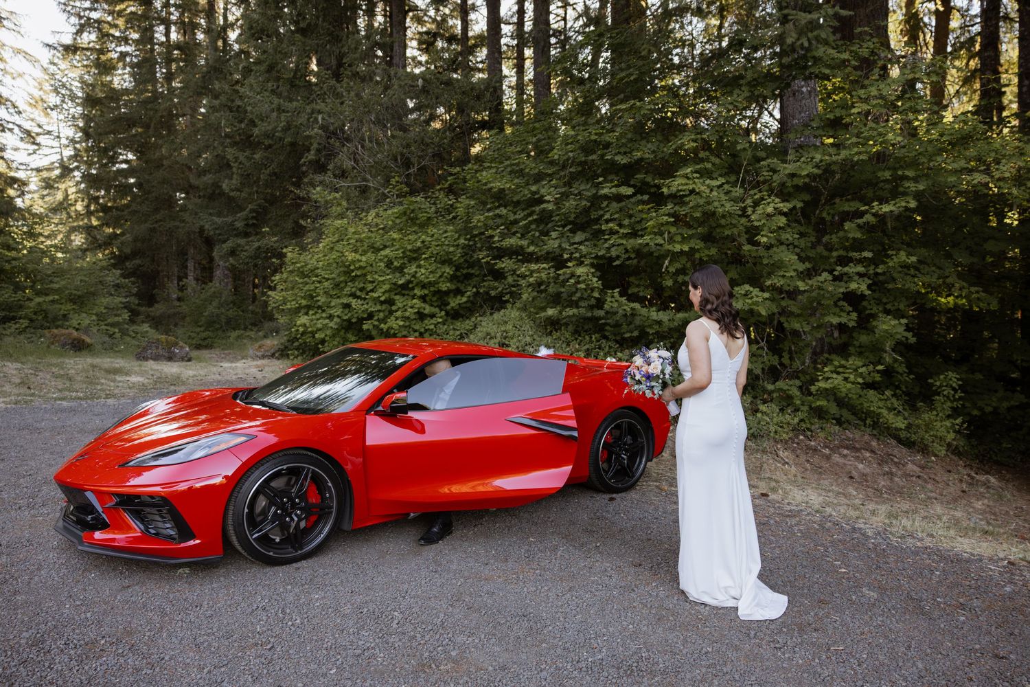 A bright red Chevrolet Corvette C8 parked on a forest road at sunset.