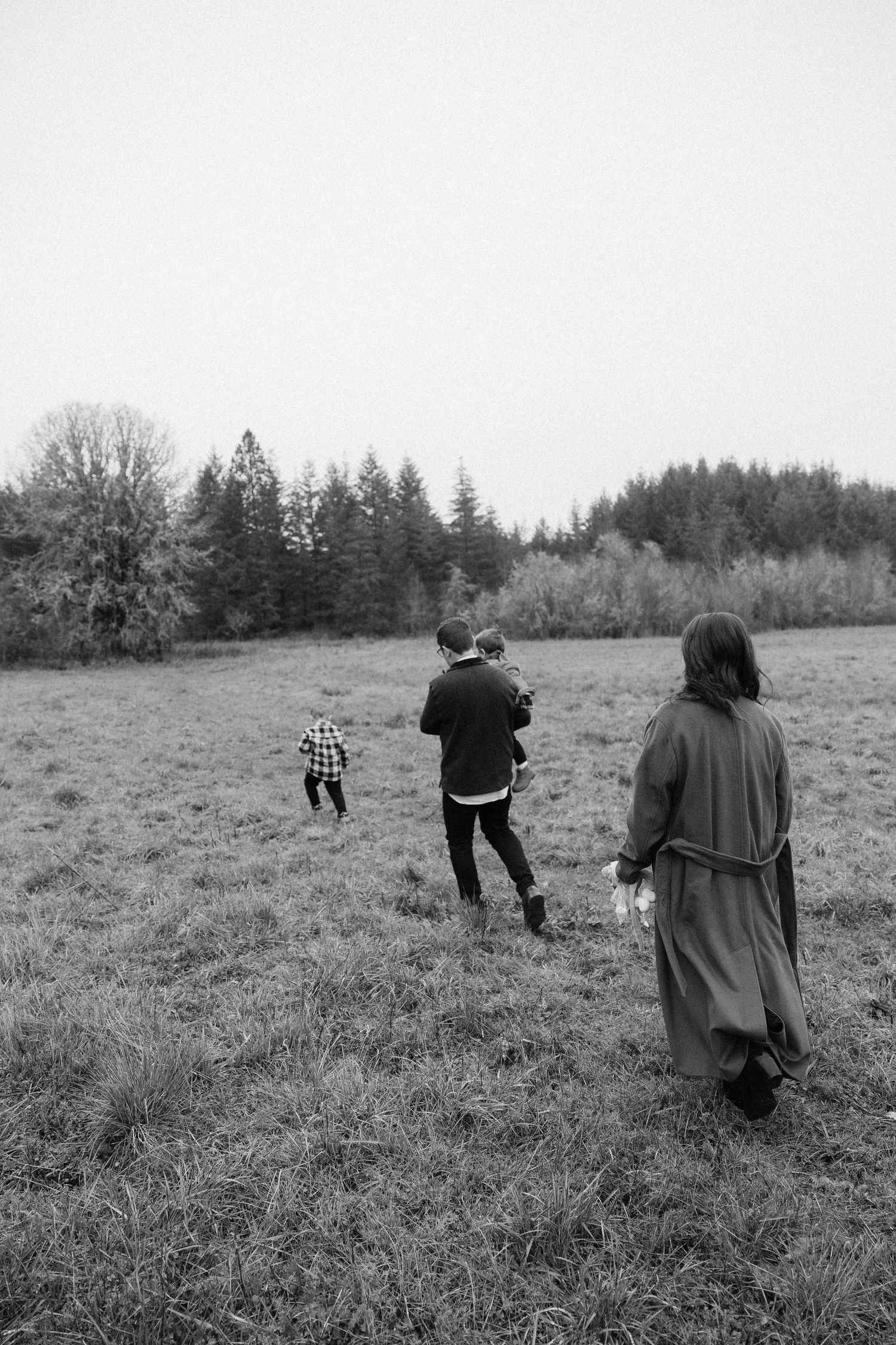 A sequence of black and white photos showing people walking across a grassy meadow with evergreen trees in the distance.