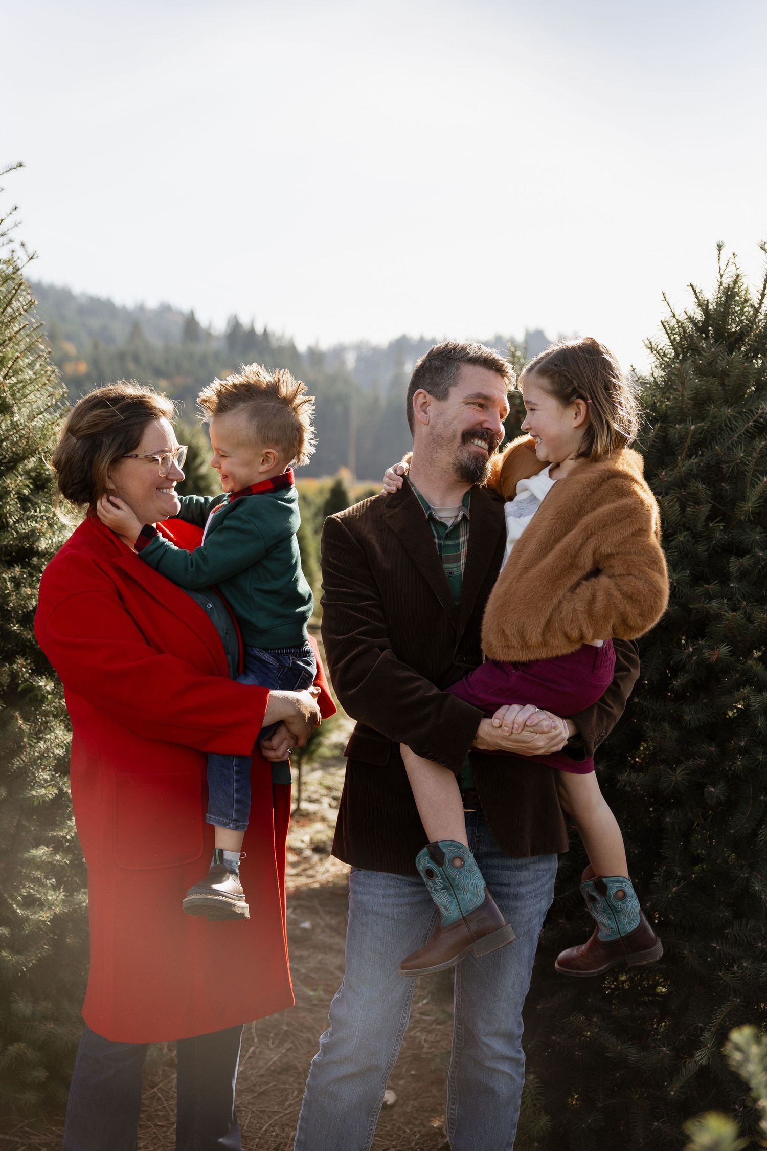Family shares playful moments together at a Christmas tree farm on a misty winter afternoon.