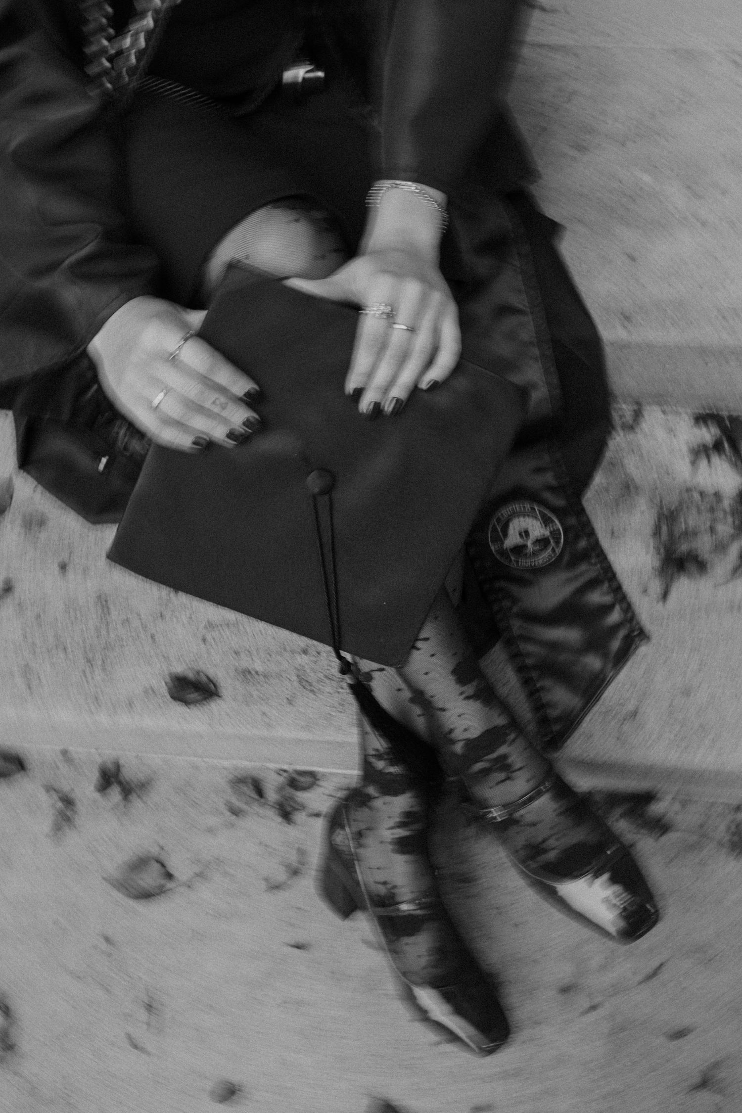 Black and white photo of hands holding a book while wearing leather boots, with fallen leaves on the ground.