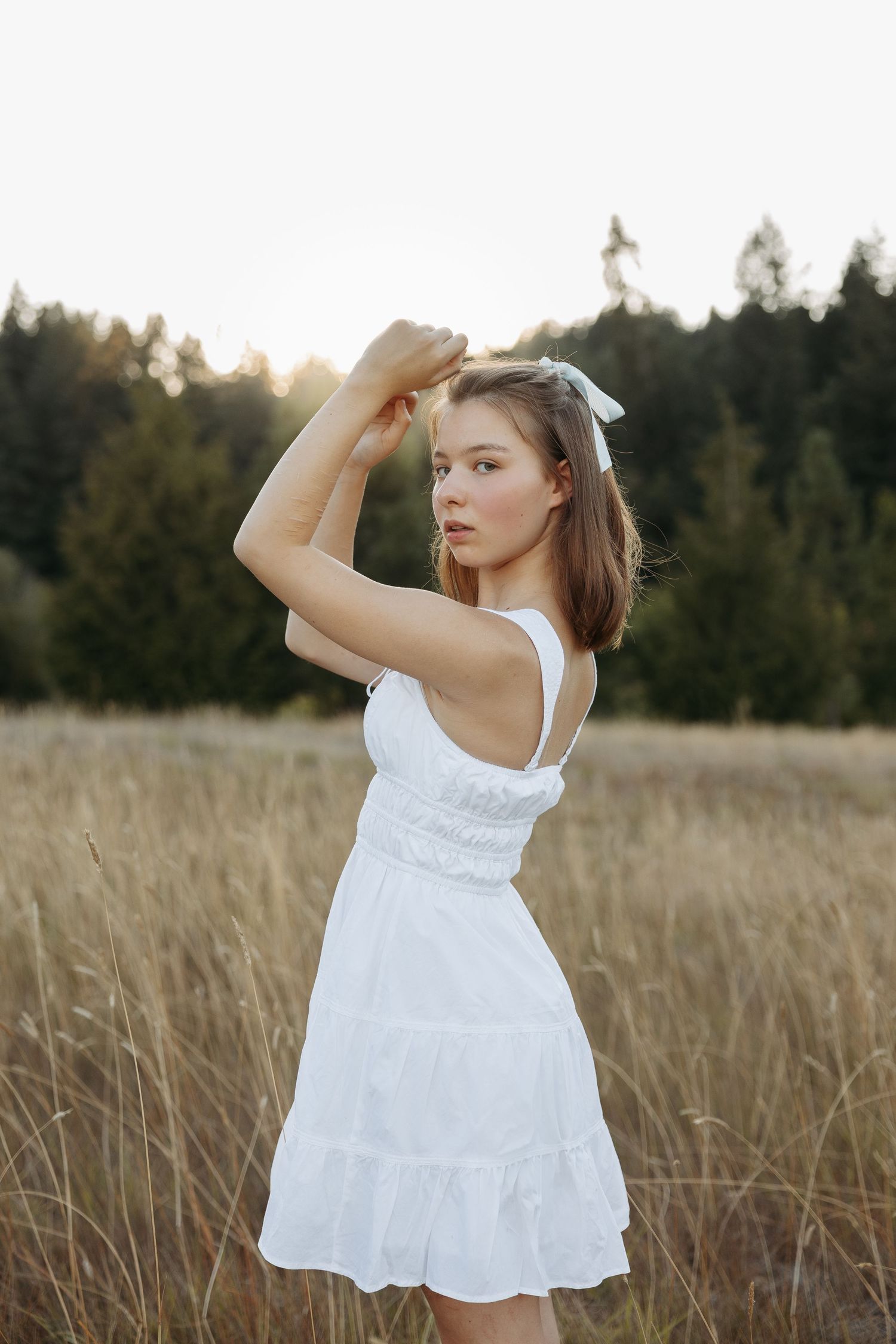 A person in a flowing white sundress poses gracefully in a golden wheat field at sunset.