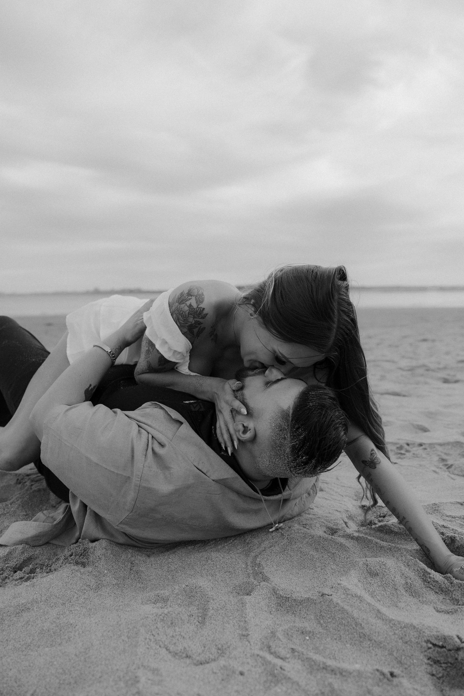 Romantic couple lying on sandy beach in black and white photography series.