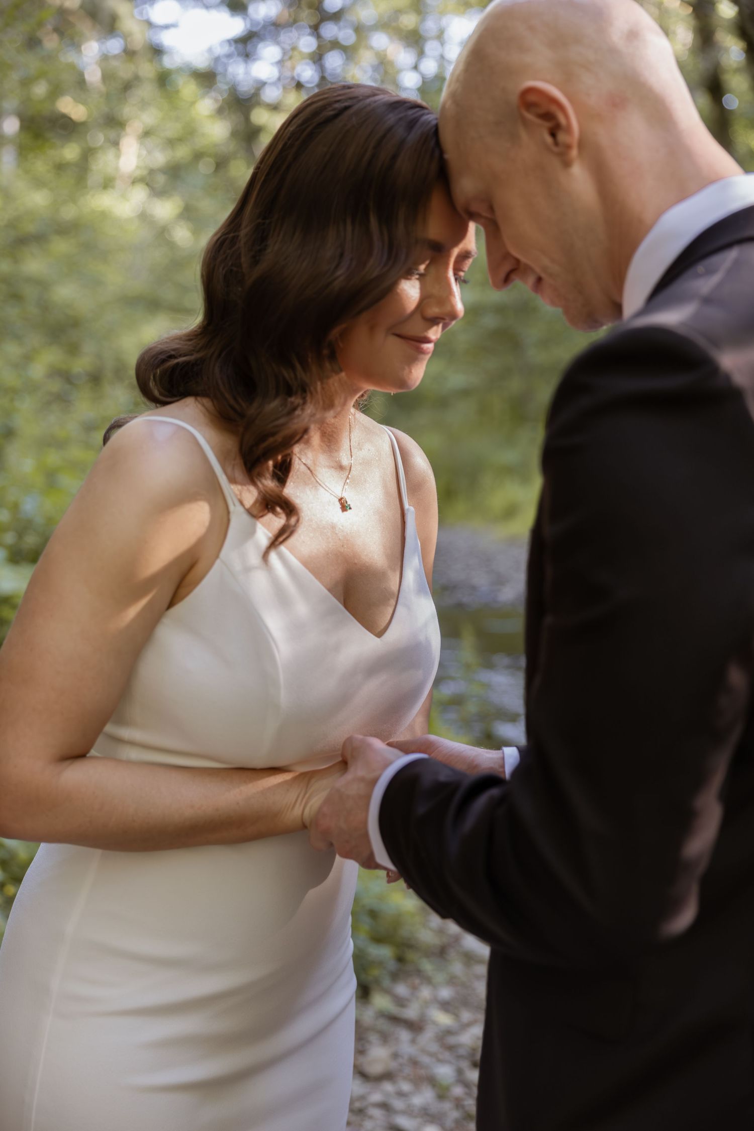 A romantic wedding couple shares an intimate dance moment in a wooded outdoor setting.