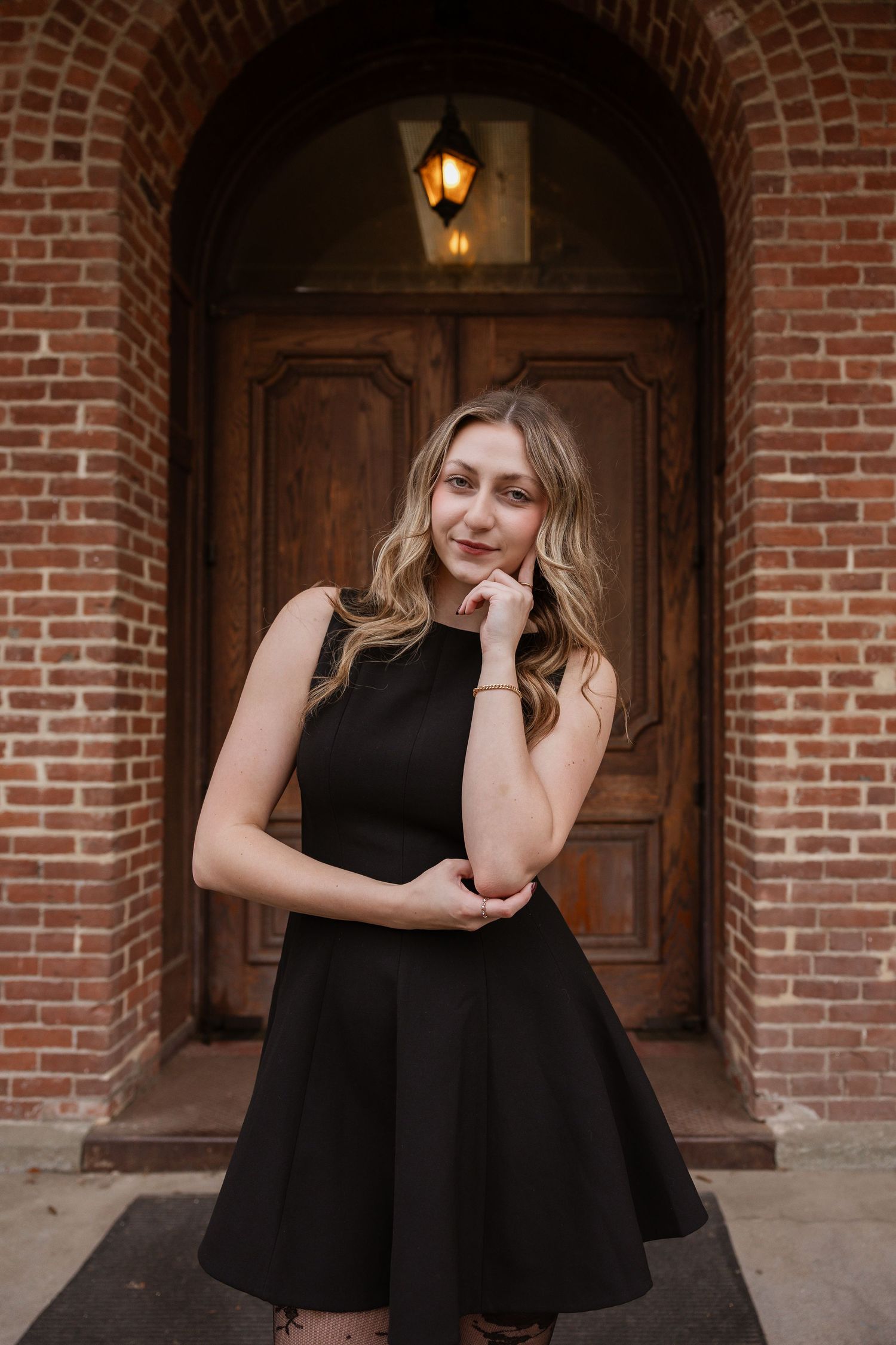 A series of four photos showing a person in a black dress posing against a brick wall with wooden doors and lanterns.