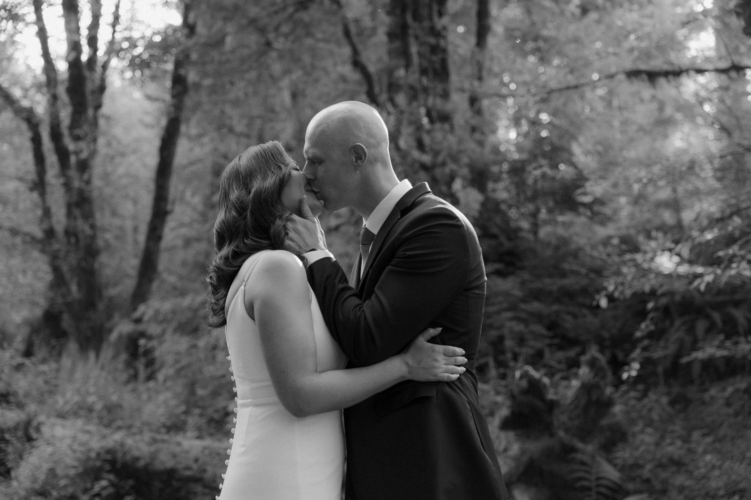 A couple shares a romantic moment in a wooded outdoor setting during a special celebration.