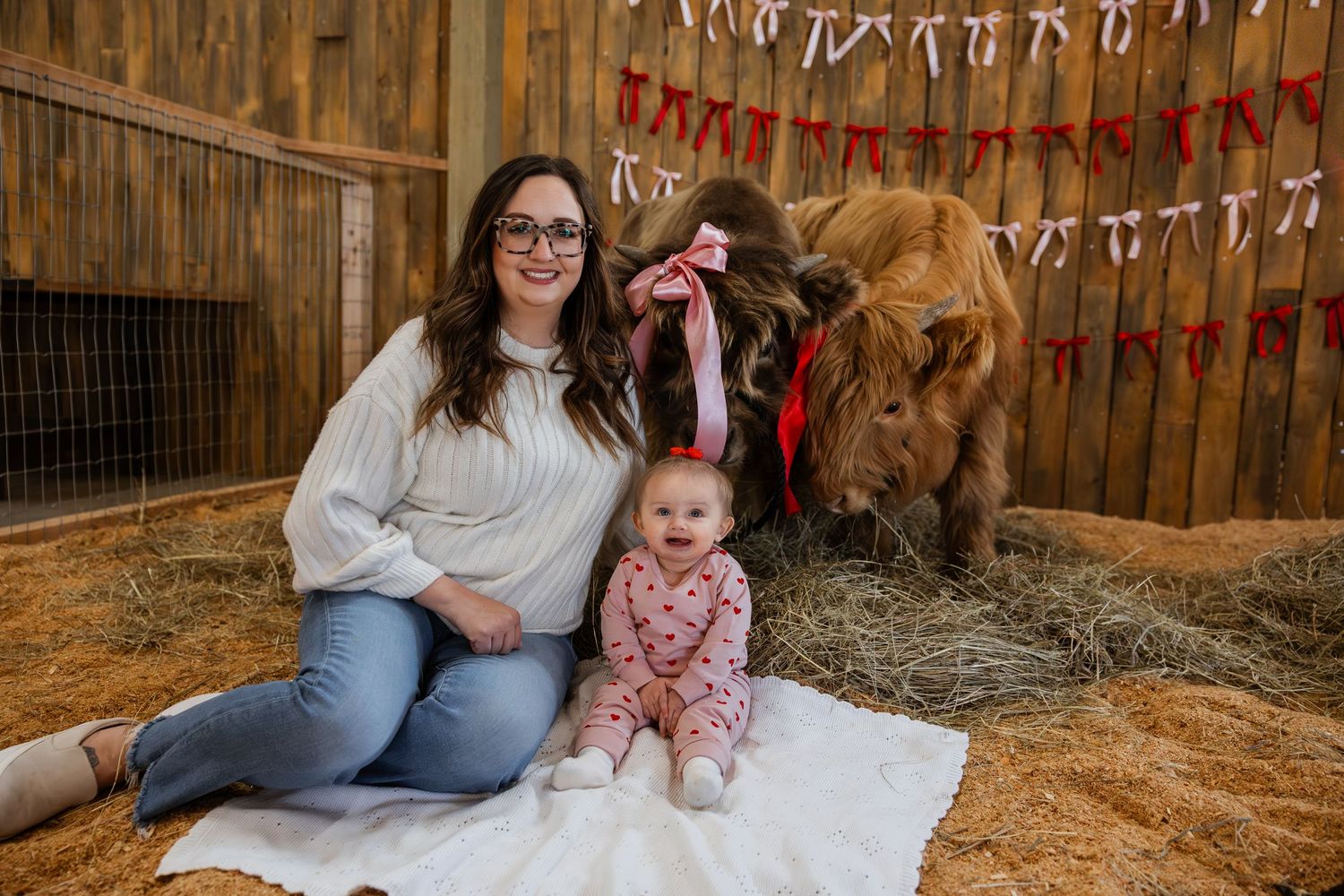Family poses together on hay bales inside a rustic barn decorated with festive holiday string lights and garland.