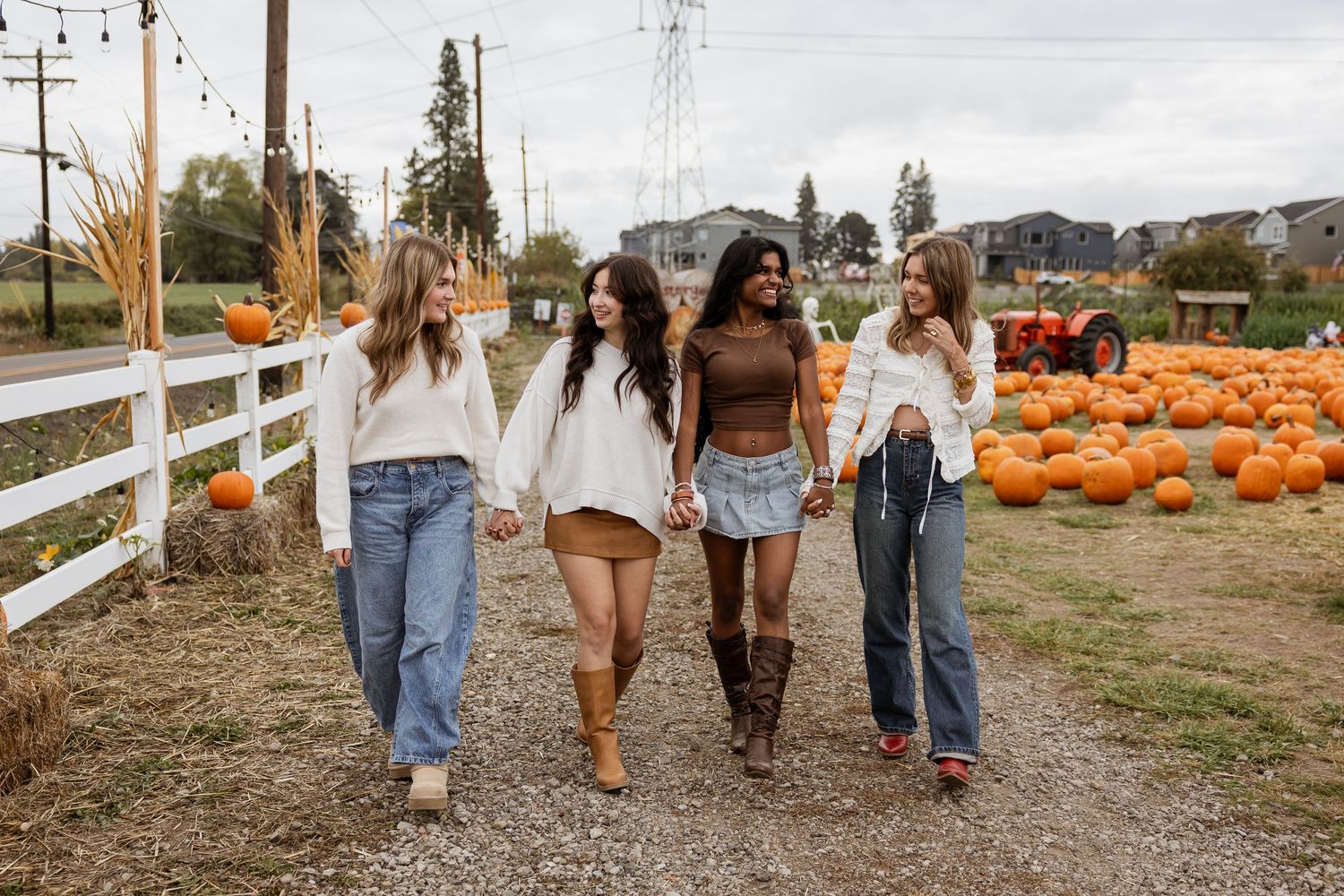 A group walks together through a rustic autumn pumpkin patch with white fencing and fall scenery.