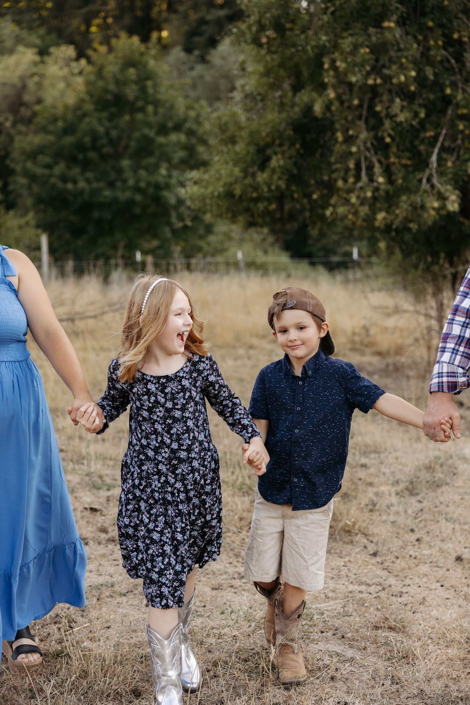 Family members holding hands while walking together in a grassy field wearing coordinated blue and navy outfits.