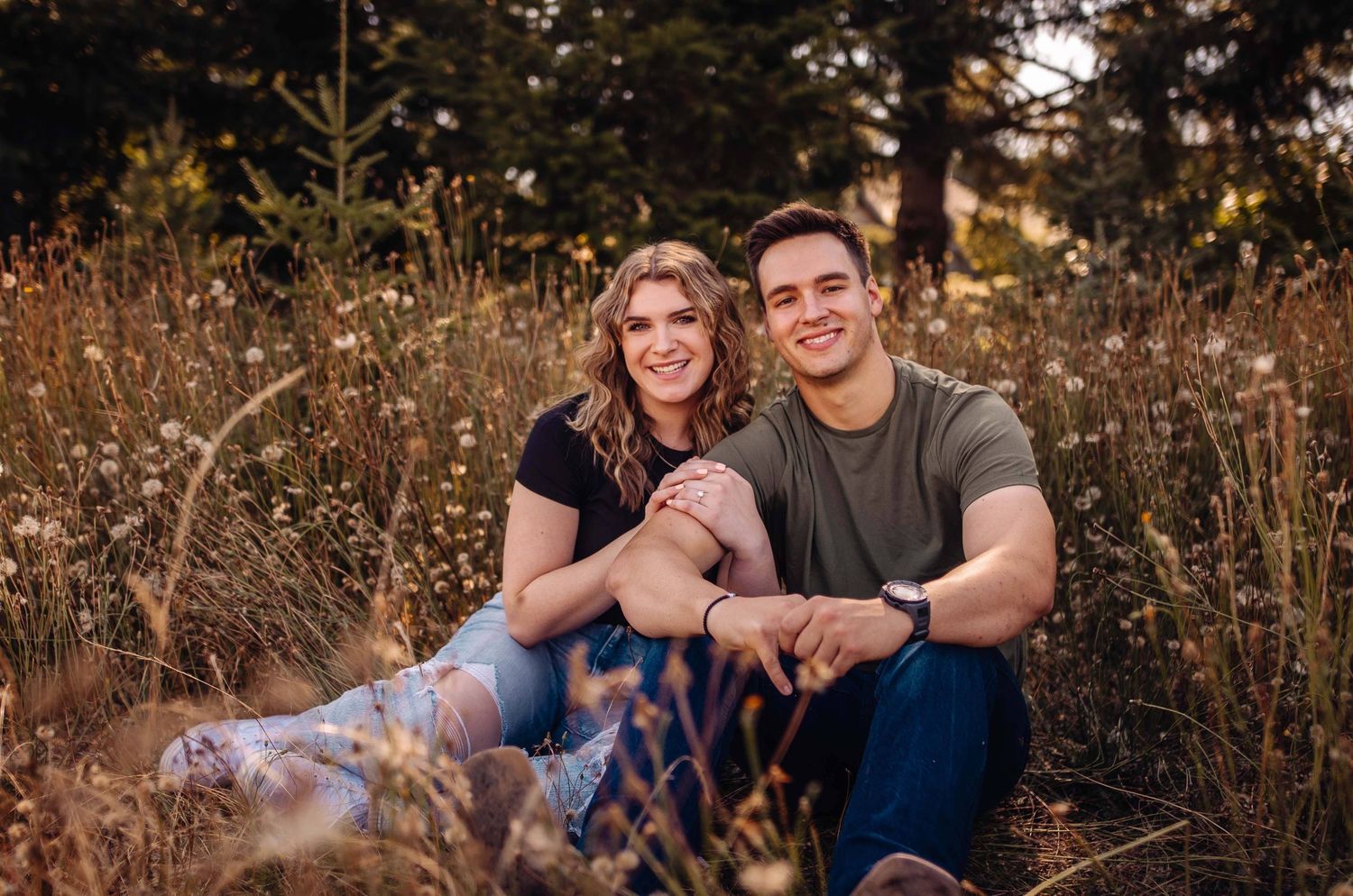 Engagement photos of couple sitting together in golden autumn field at sunset.