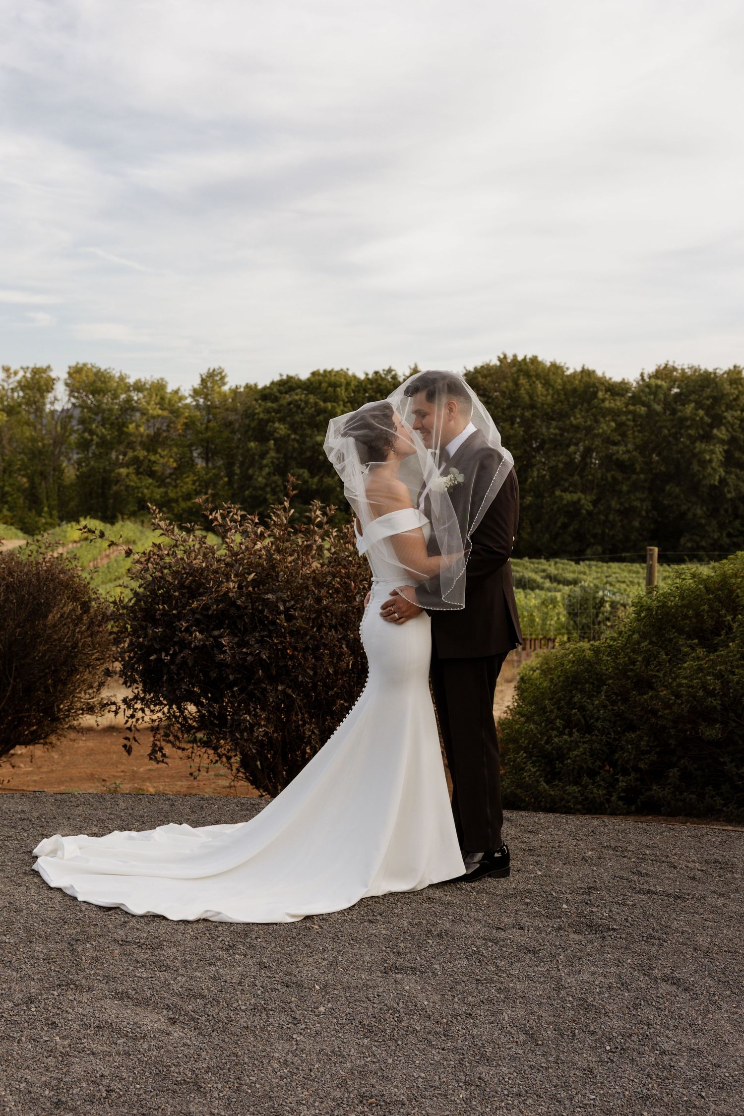 Romantic wedding couple embracing on a path with dramatic veil flowing in the wind.
