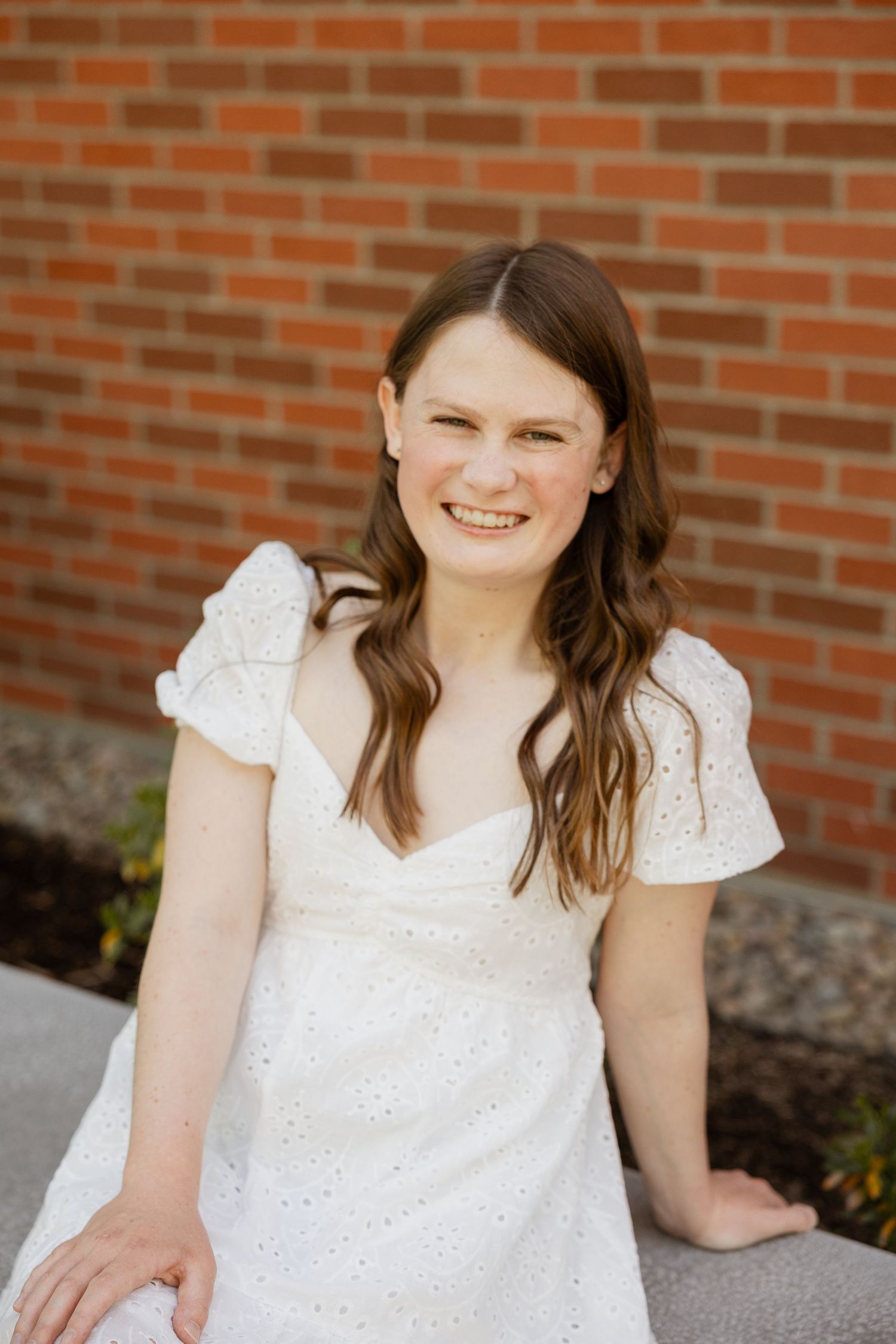 A series of four portrait photos showing someone in a white eyelet dress against a brick wall background.