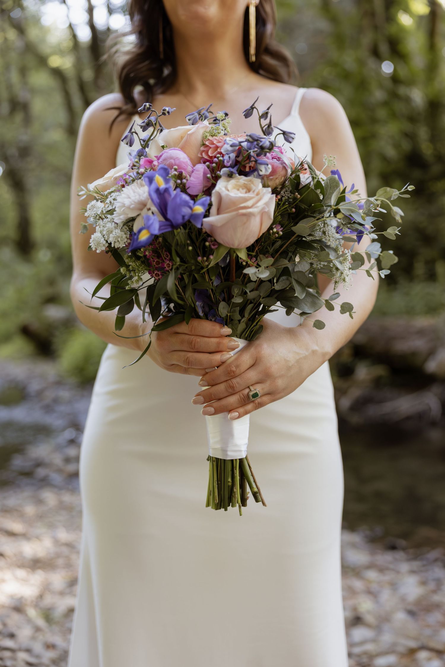 A beautiful wedding bouquet with purple and pink flowers held against a white bridal gown.