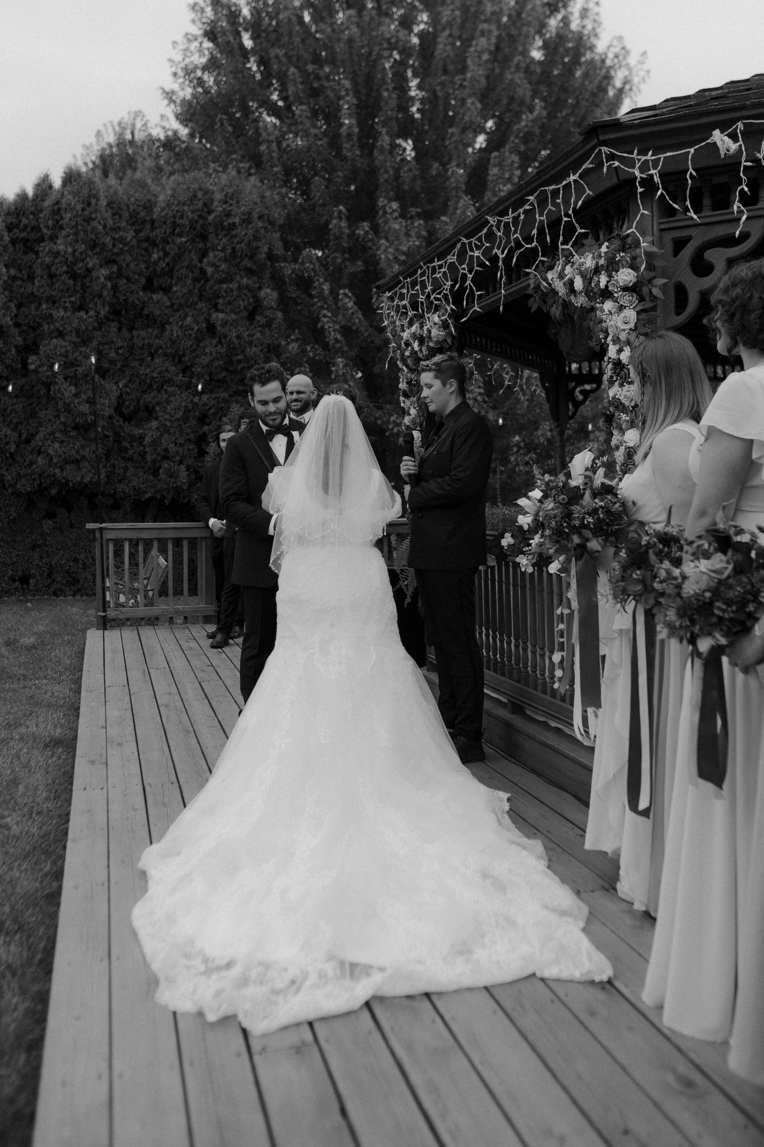 Wedding ceremony scene on wooden deck with flowing white dress and purple bridesmaid dresses.