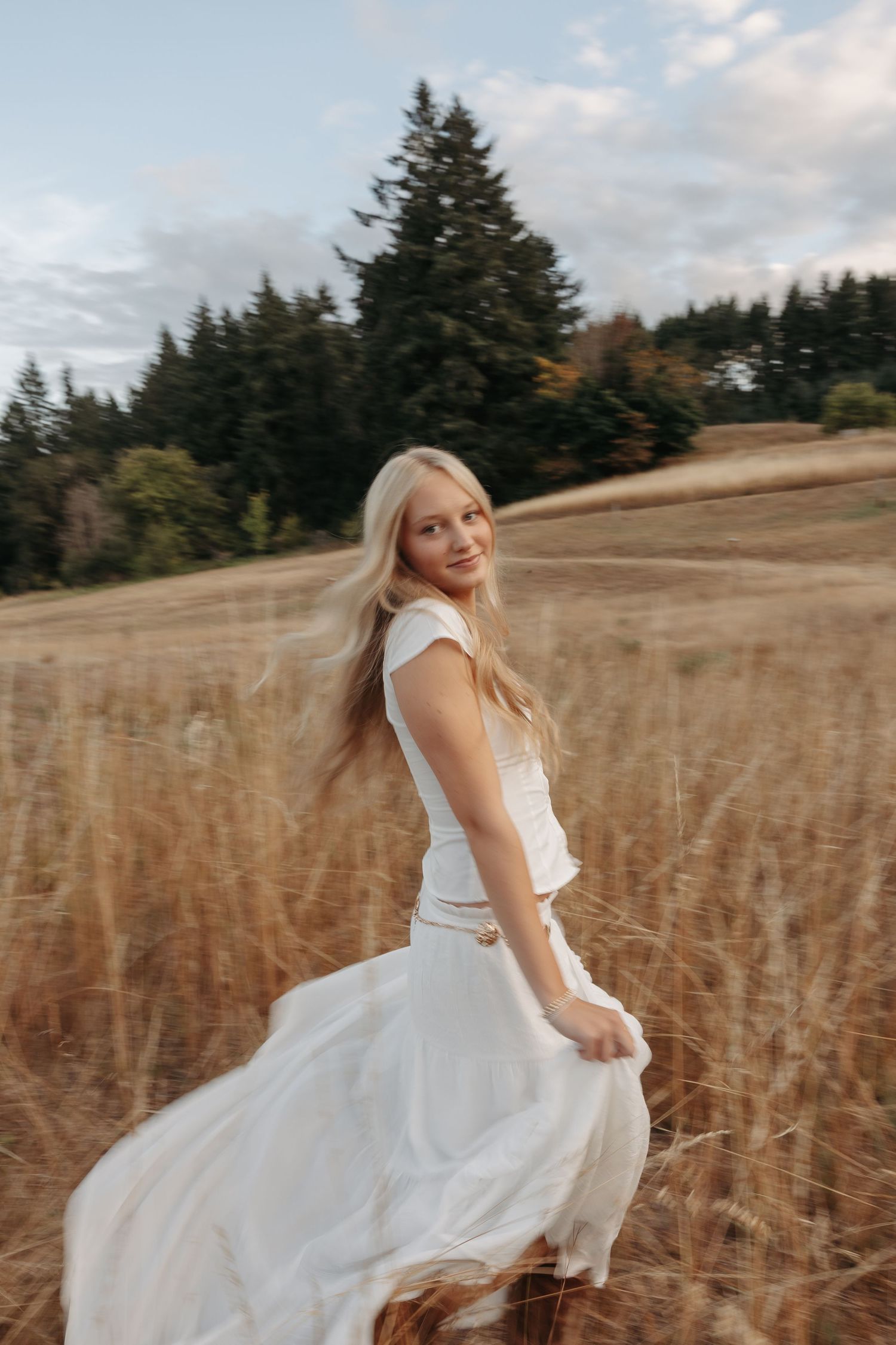 A person in a flowing white dress twirls through a golden field of tall grass at sunset.