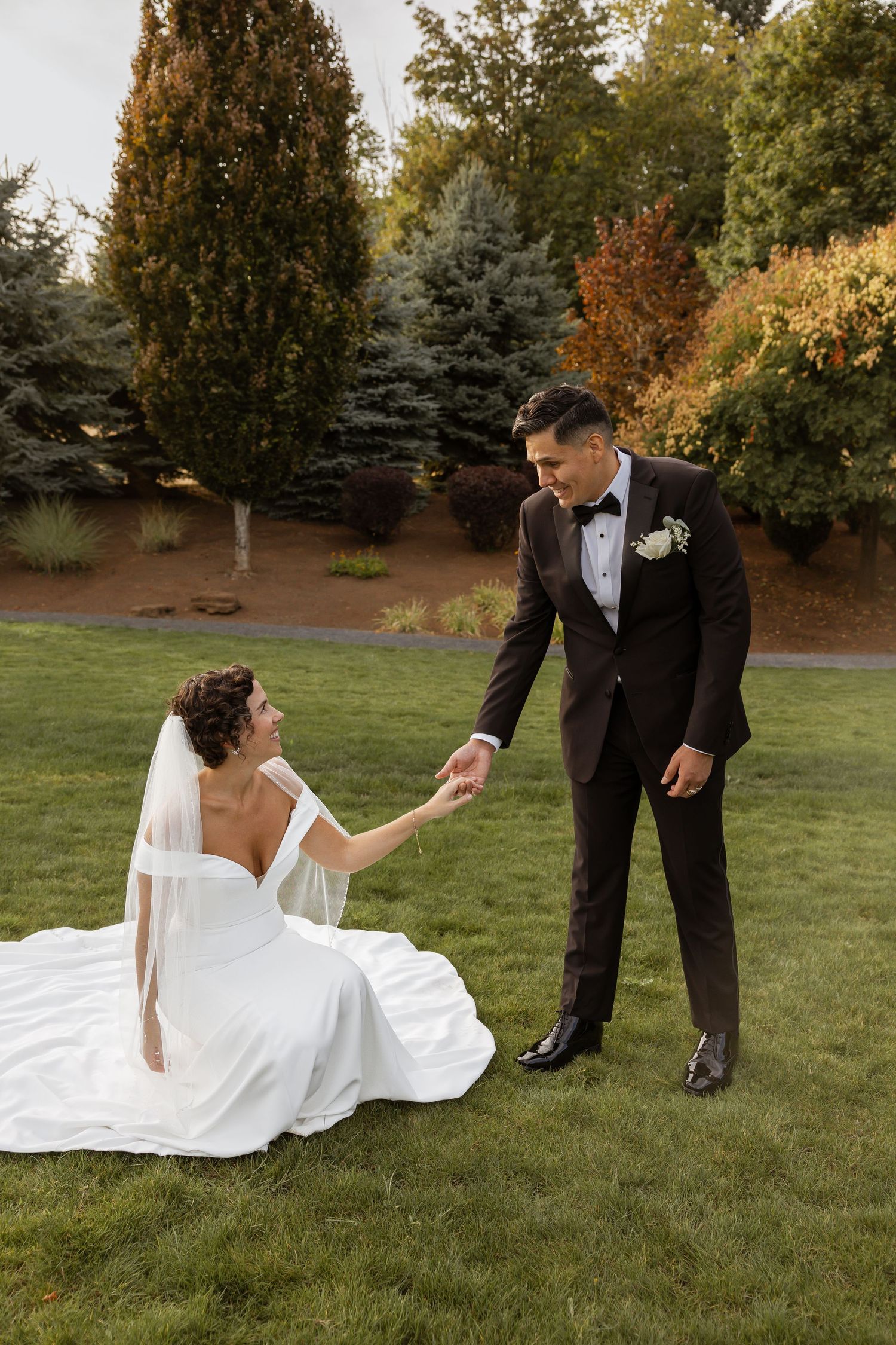 Playful wedding couple interacting on grassy lawn with autumn trees in background.