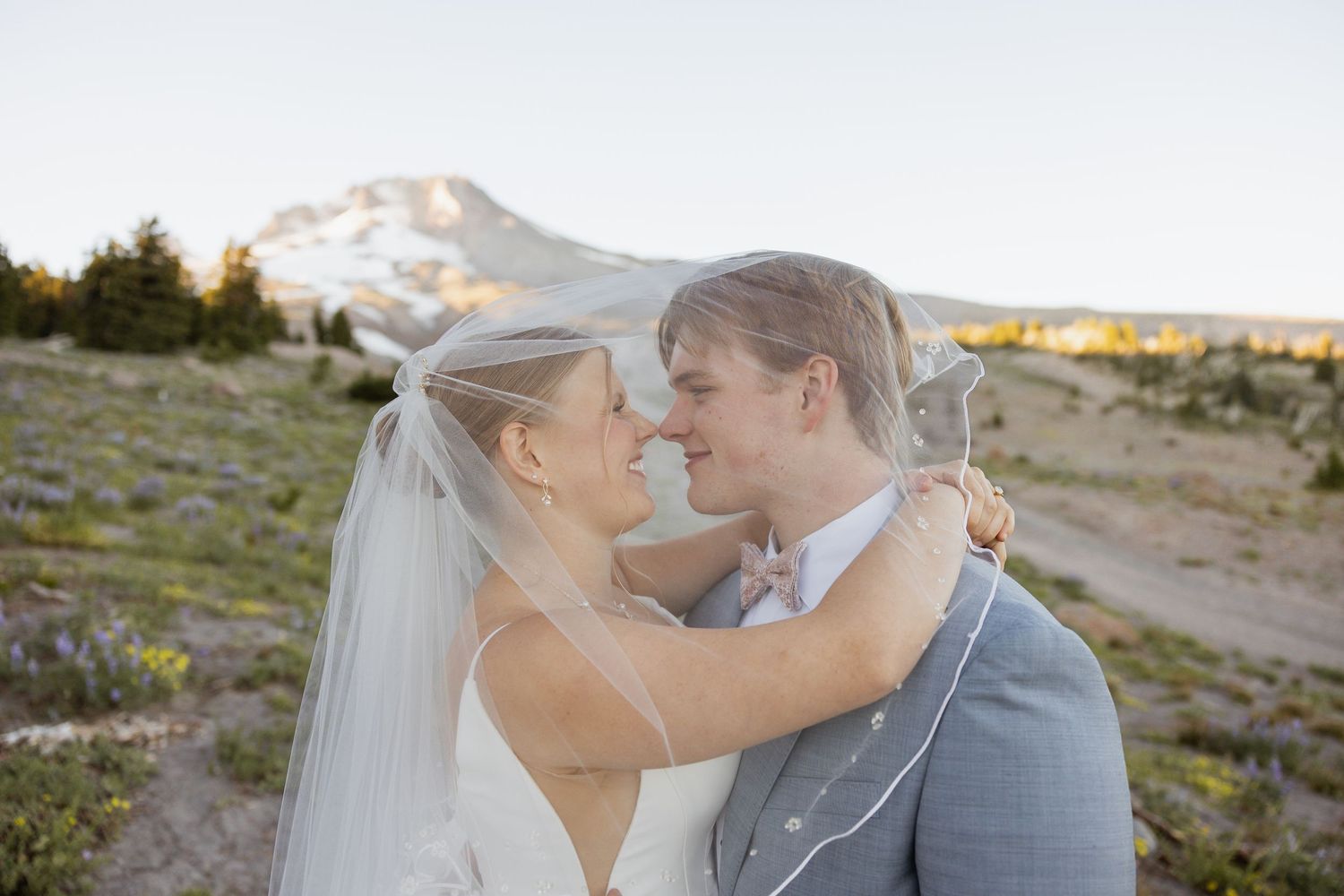 A romantic wedding couple embraces on a scenic mountainside at sunset.