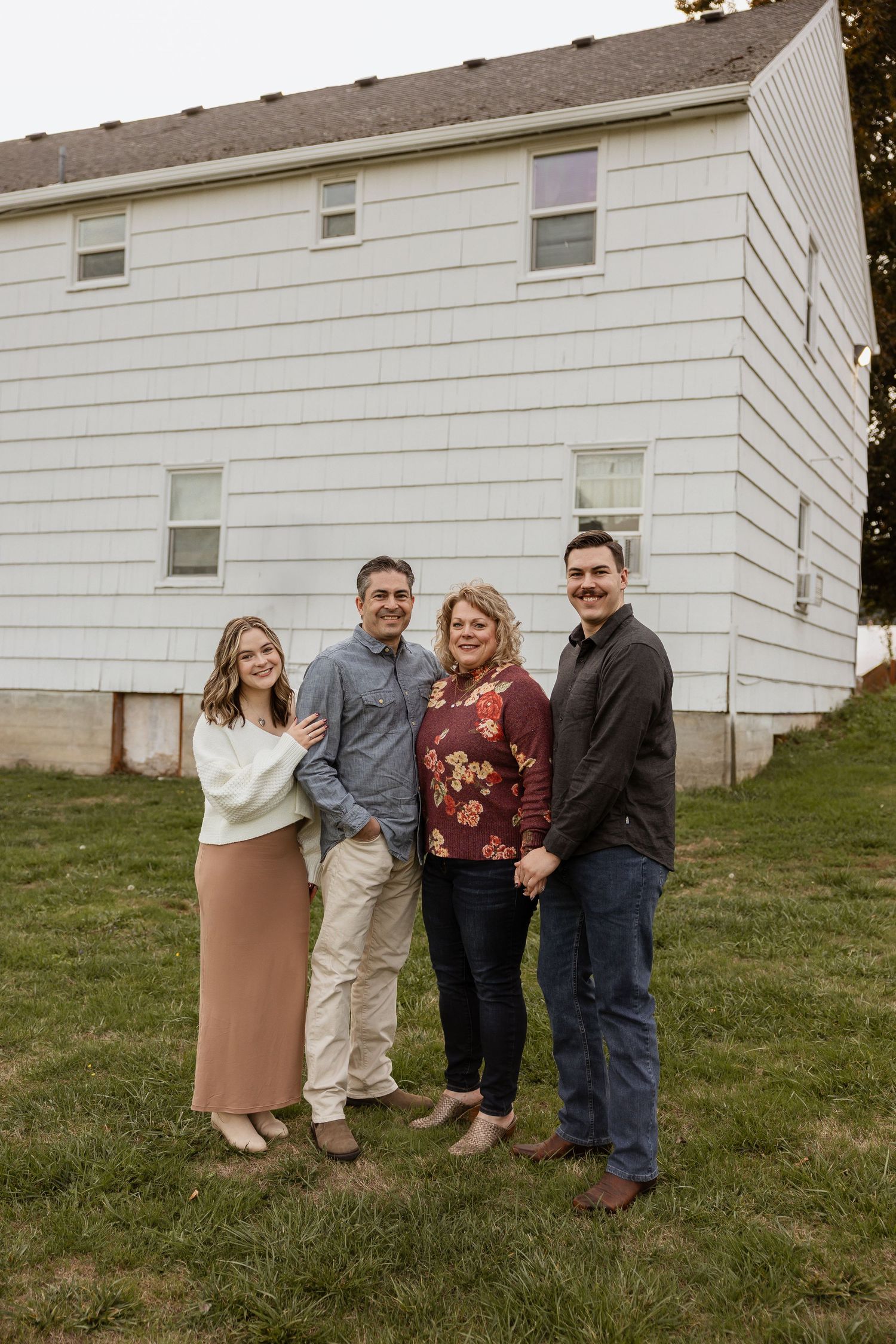 A group of people pose together on a grassy hillside next to a white building.