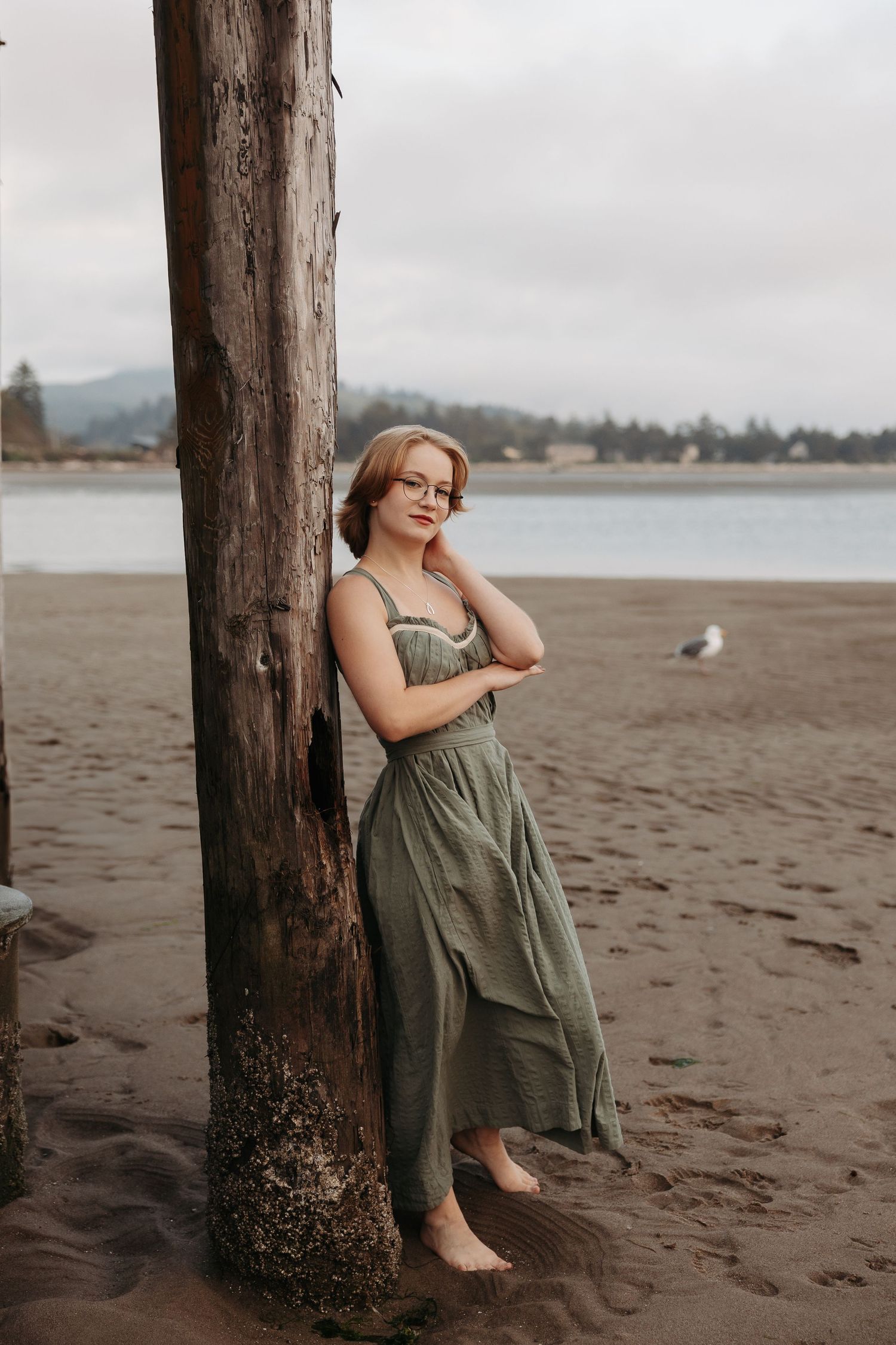 A series of beach portraits showing someone in an olive green dress leaning against a wooden post on a sandy shore.