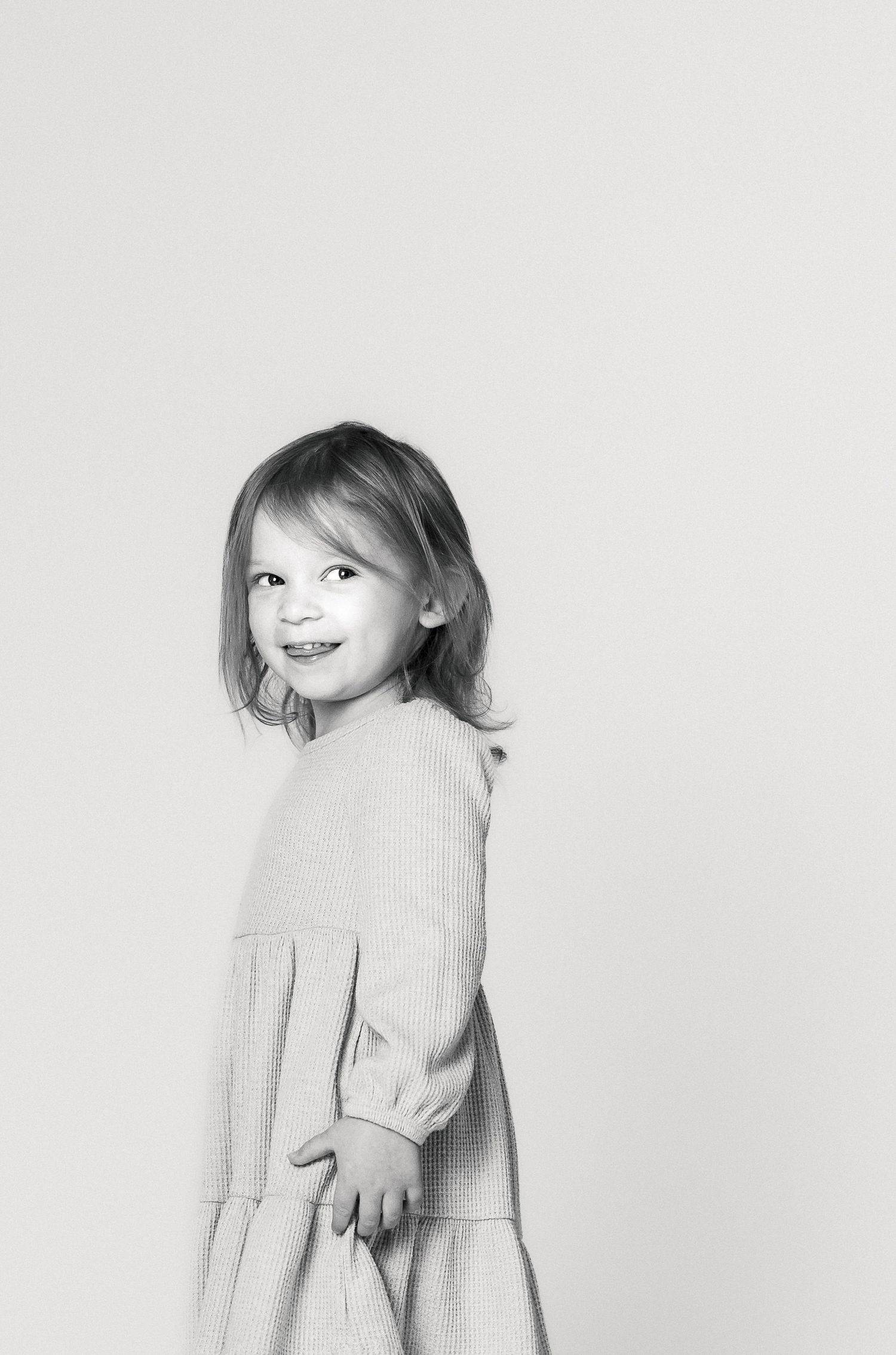 A young girl with blonde hair smiling at the camera against a plain white background.