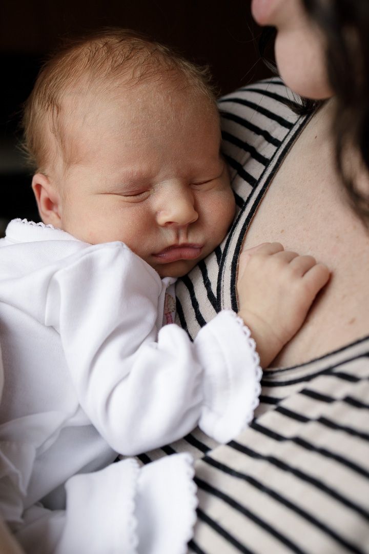 Sleeping infant in white clothing resting against striped fabric in soft lighting.