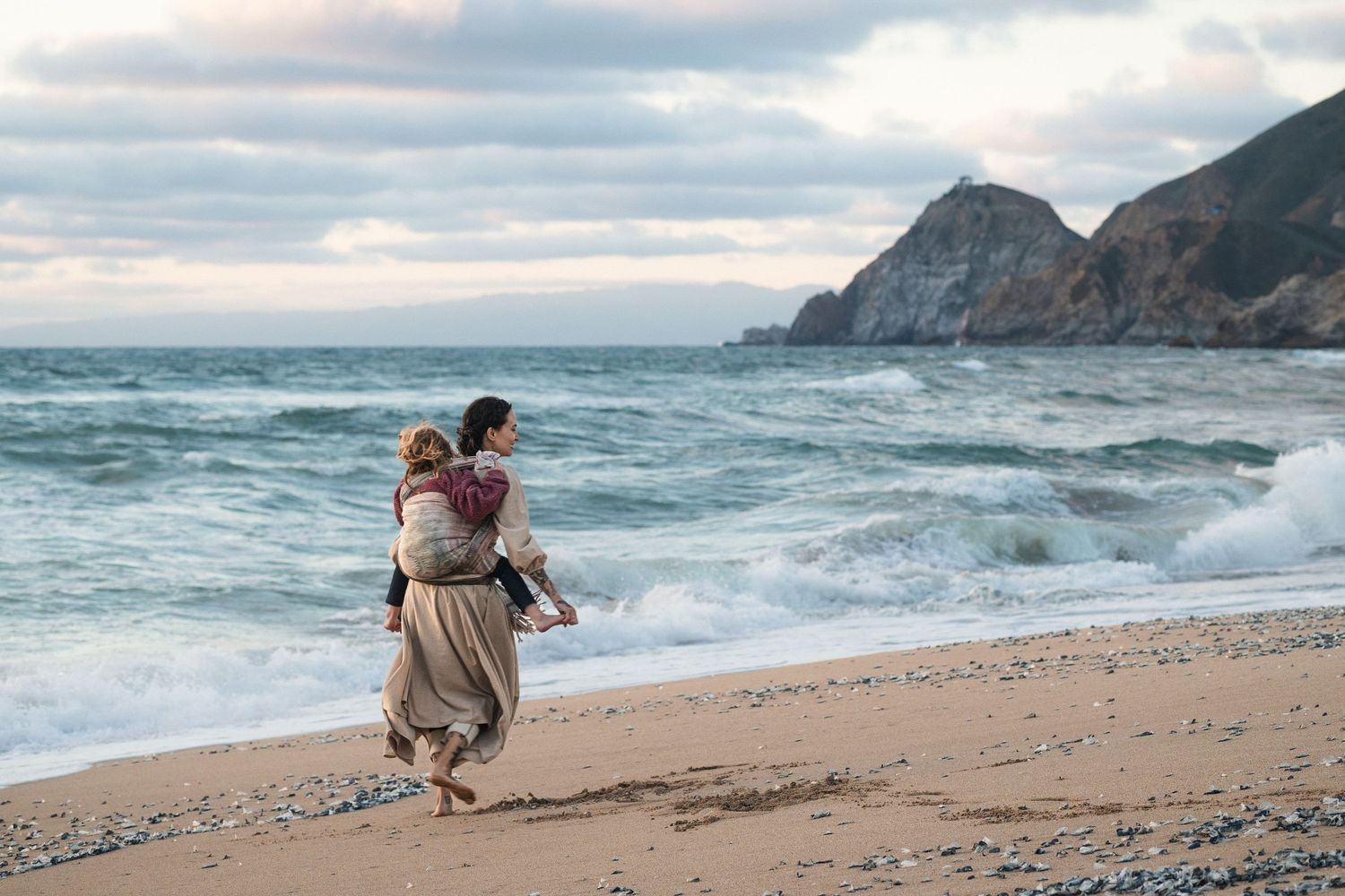 Couple walking on a rocky beach with crashing waves and dramatic cliffs in the background.