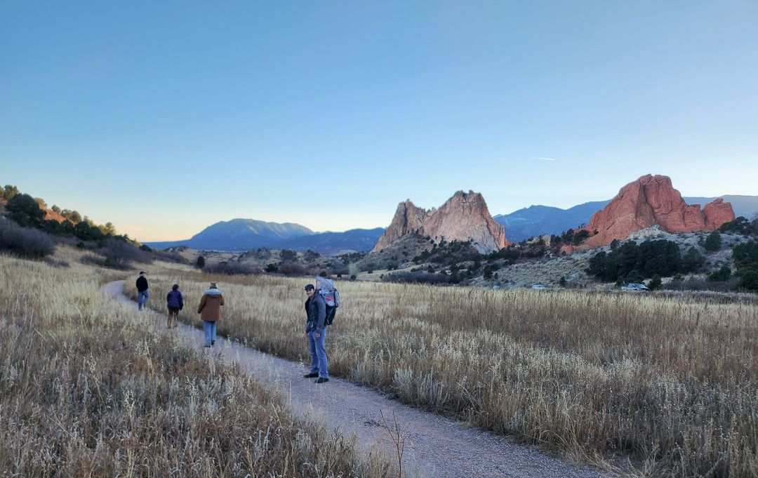 Family hikes through scenic red rock formations and mountains in the background at Garden of the Gods in Colorado