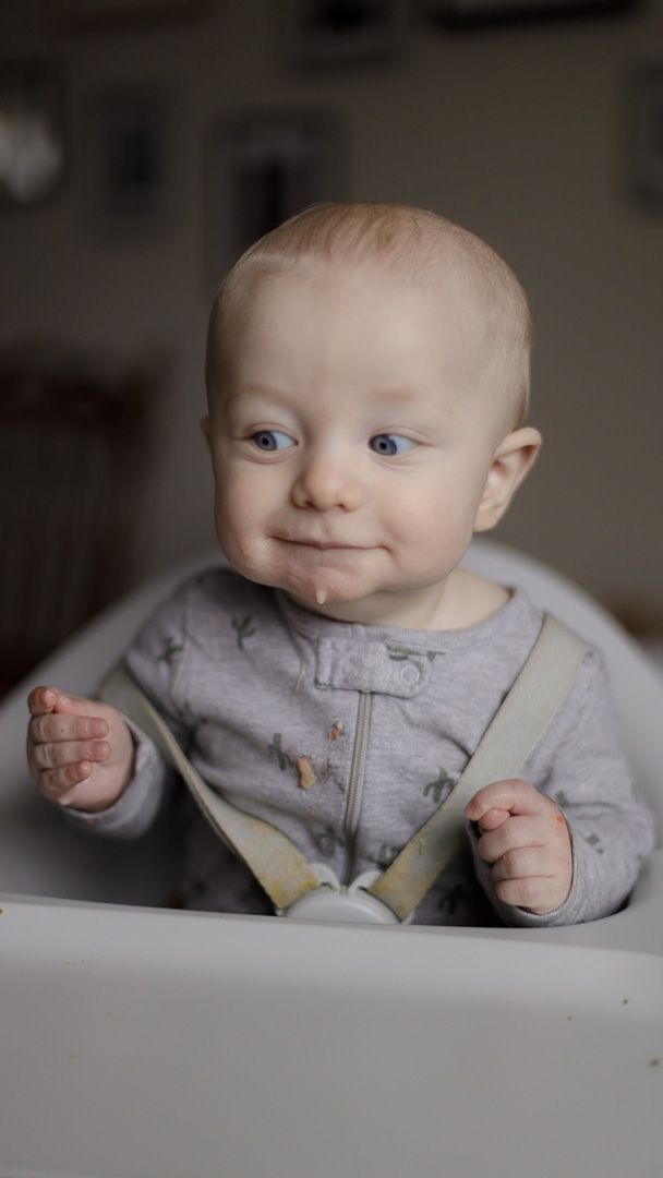 Baby in grey outfit showing animated expressions while sitting at white table.