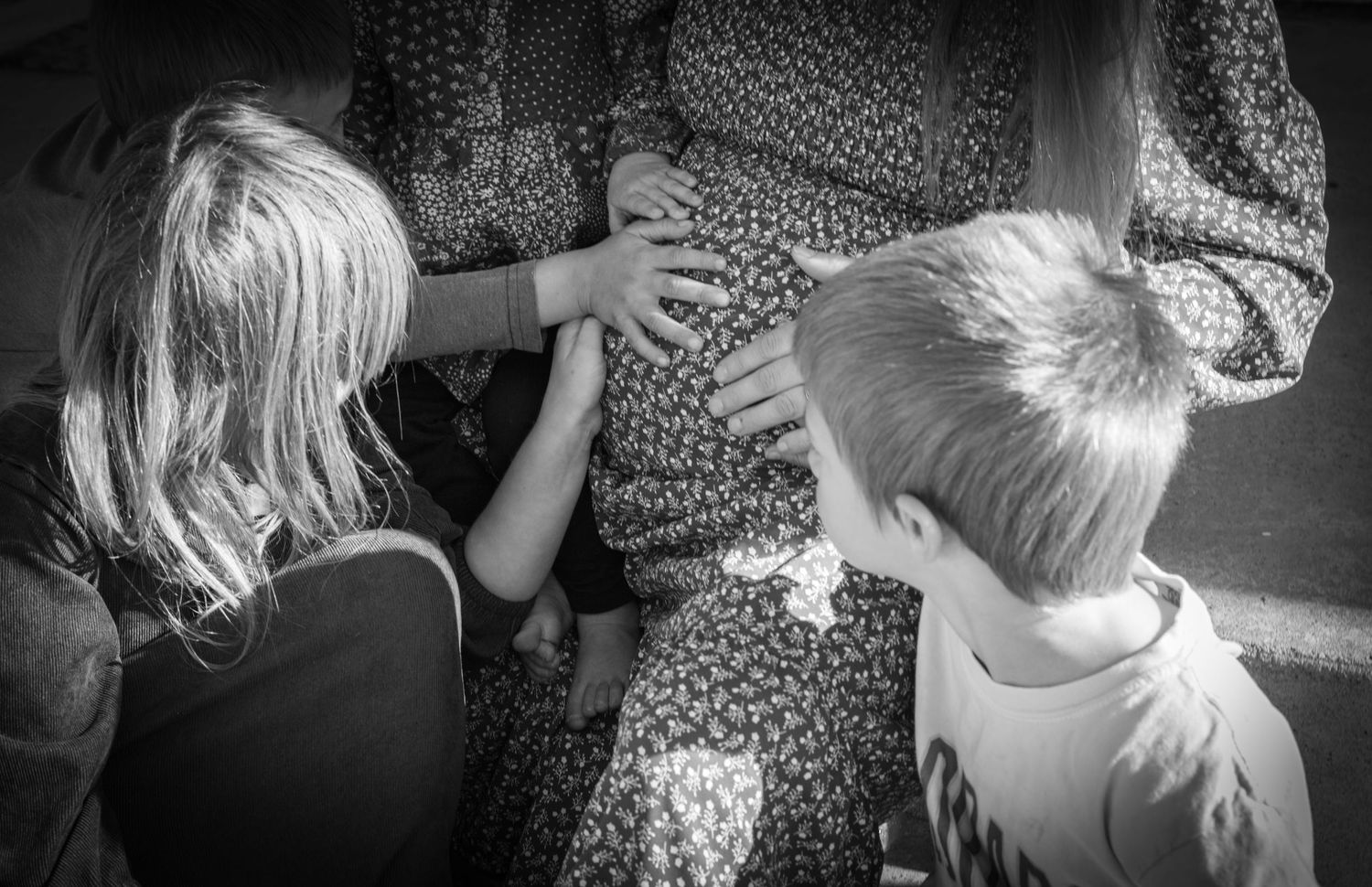 A sequence of intimate family interactions captured in dramatic black and white lighting. Children touch mothers pregnant belly.