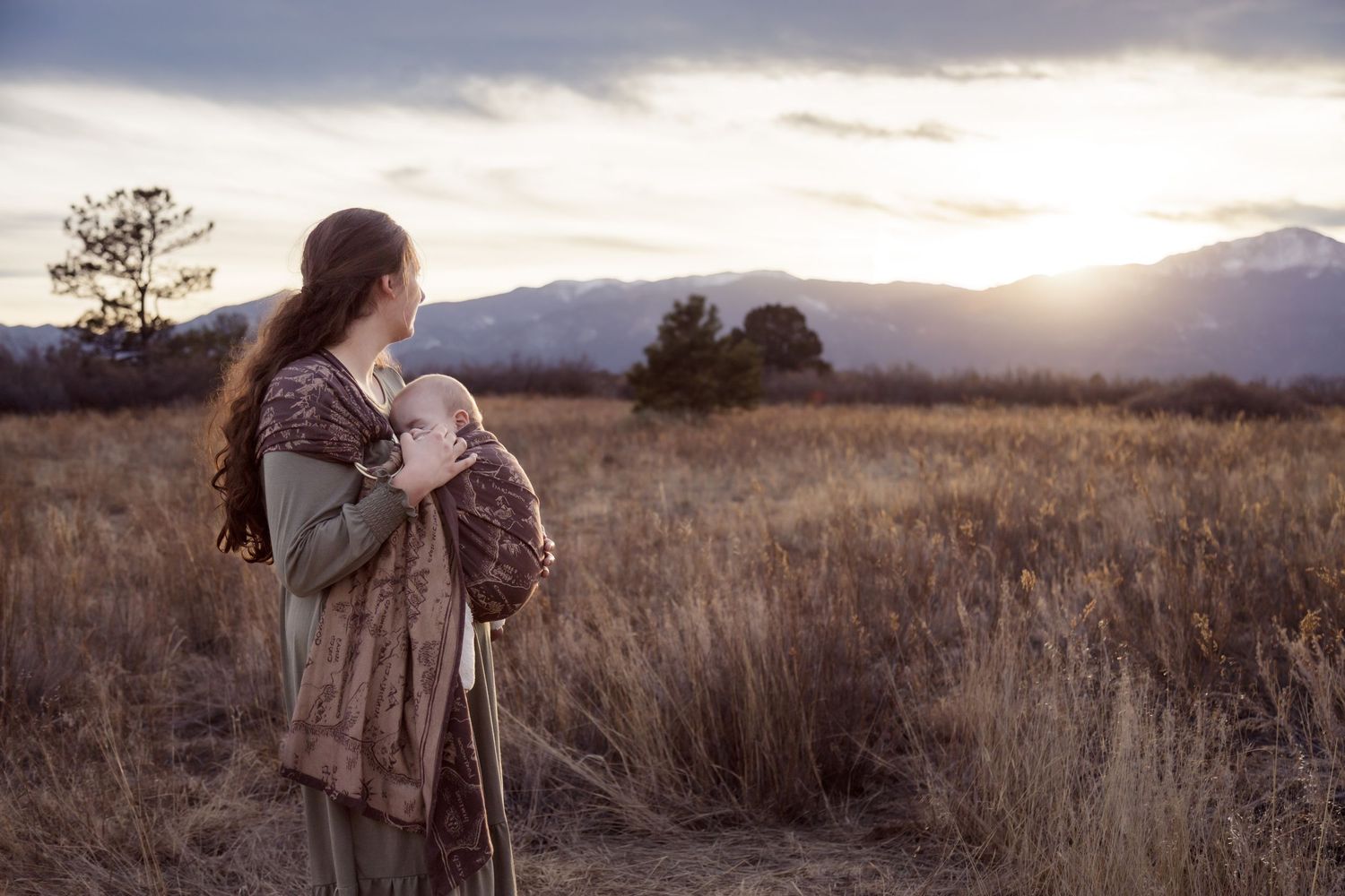 Editorial lifestyle babywearing photo of a mom and baby at Pikes Peak sunset, featuring an Oscha Slings Middle-earth collection wrap