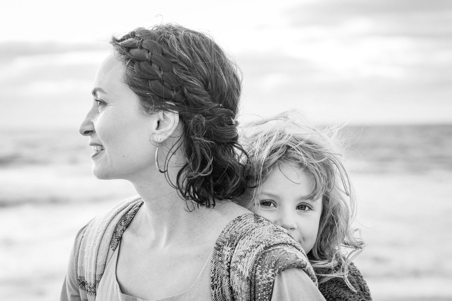 Black and white photo of a smiling woman with braided hair holding a young child at the beach.