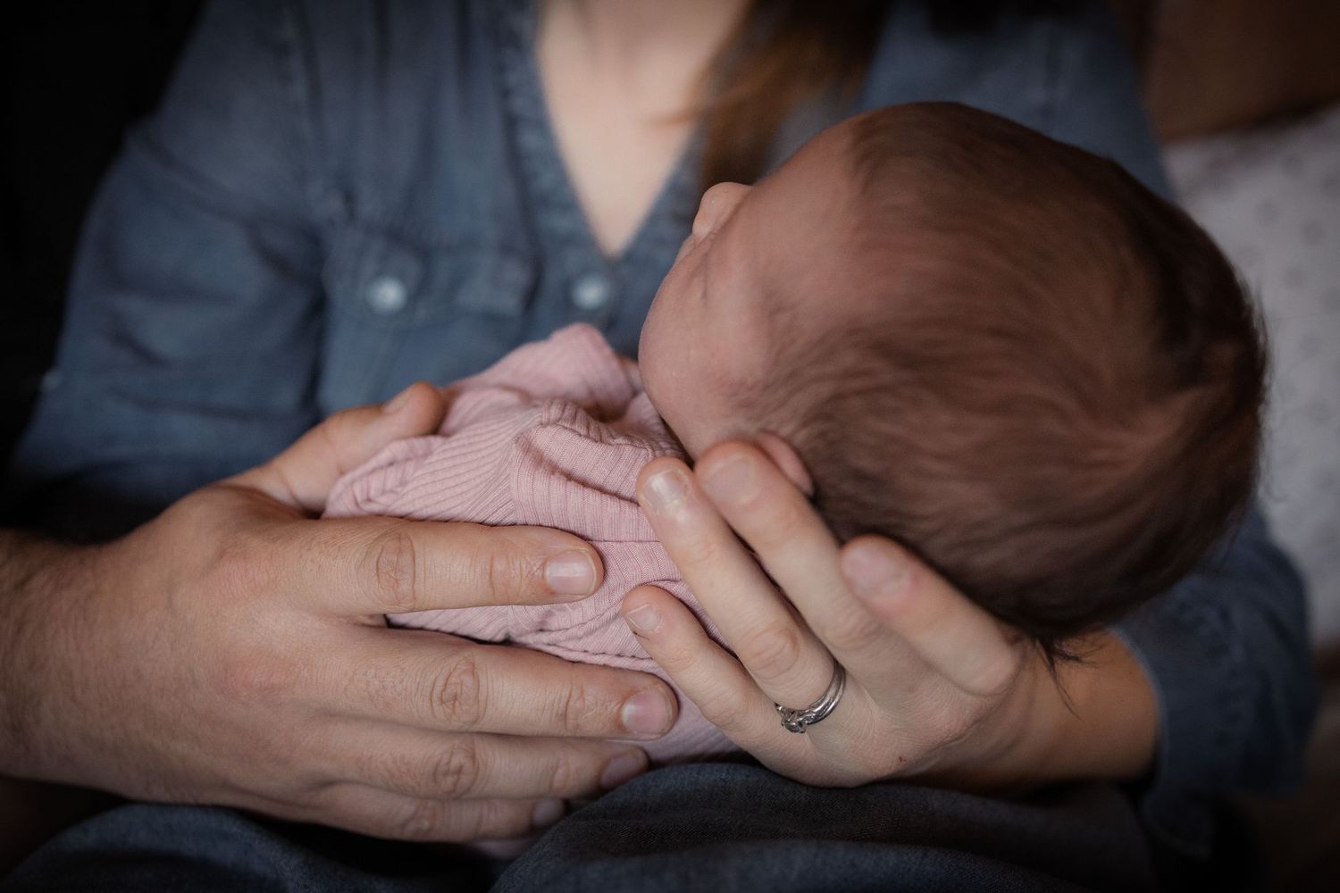 A series of hands holding and supporting a newborn baby in various gentle poses against a dark background.
