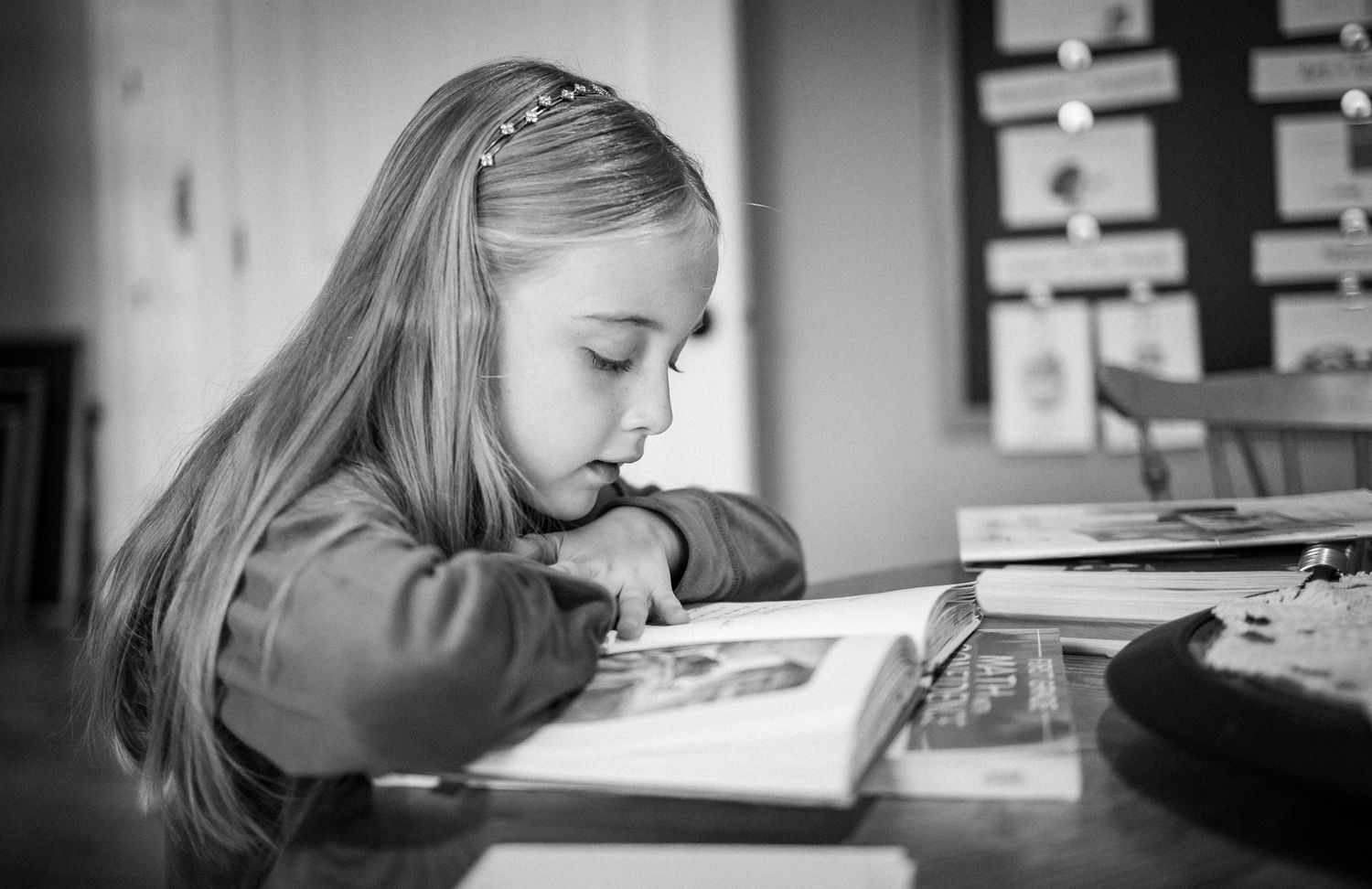 A young girl concentrates while reading a book at their desk in black and white photography during homeschooling