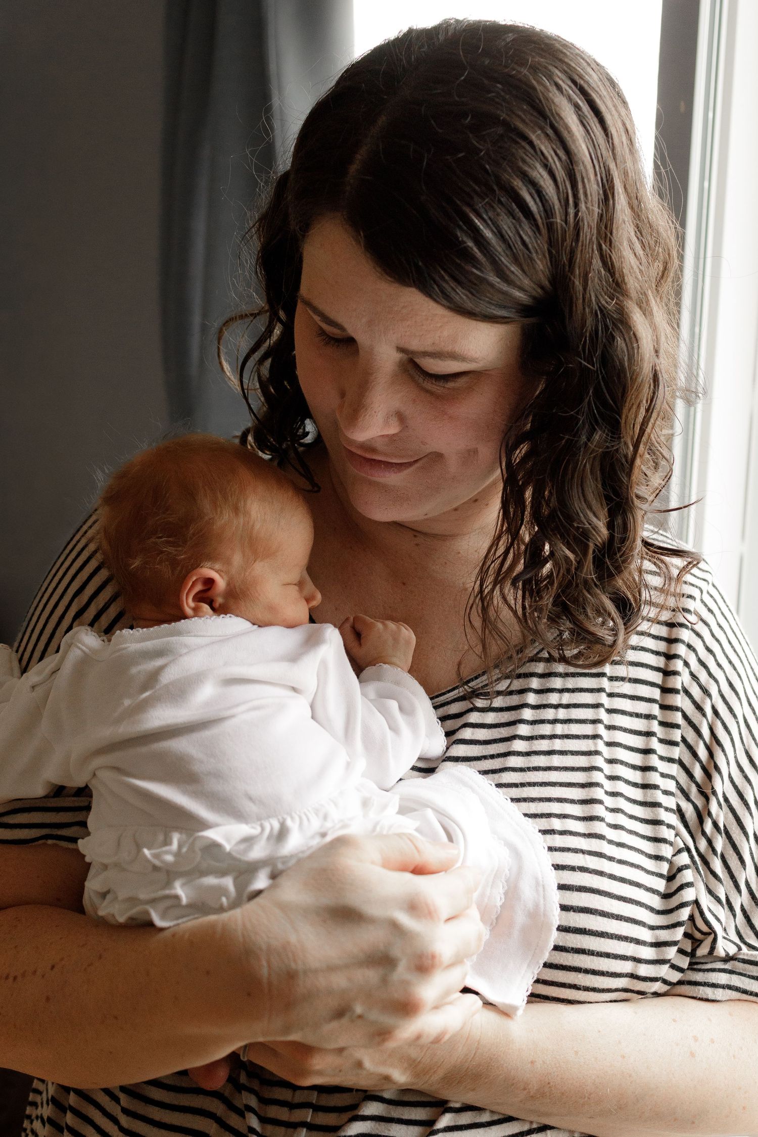 A tender moment showing someone in a striped shirt holding and gazing lovingly at a newborn baby.
