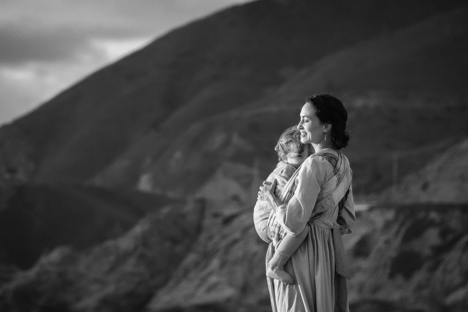 Black and white photo of a mother tenderly holding her child with mountain landscape in the background.