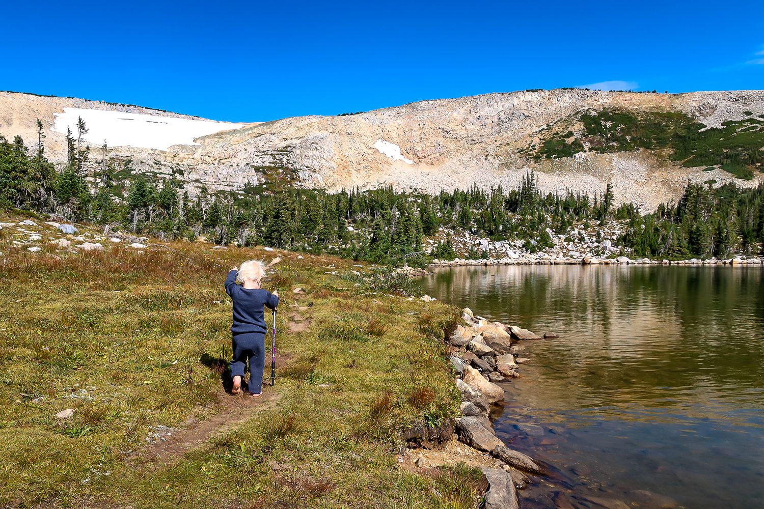 Hikers explore scenic mountain trails and alpine lakes in a rugged wilderness landscape under clear blue skies.