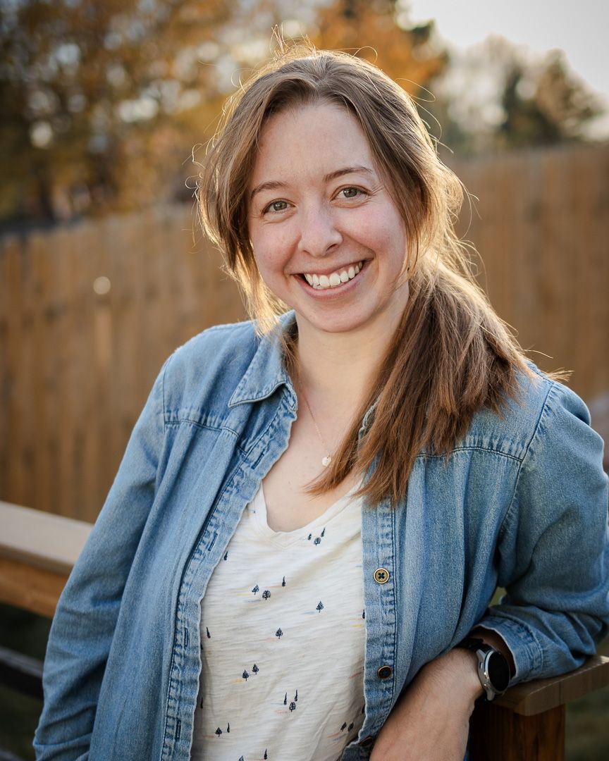 Person in denim jacket and white shirt sitting outdoors during golden hour autumn lighting.