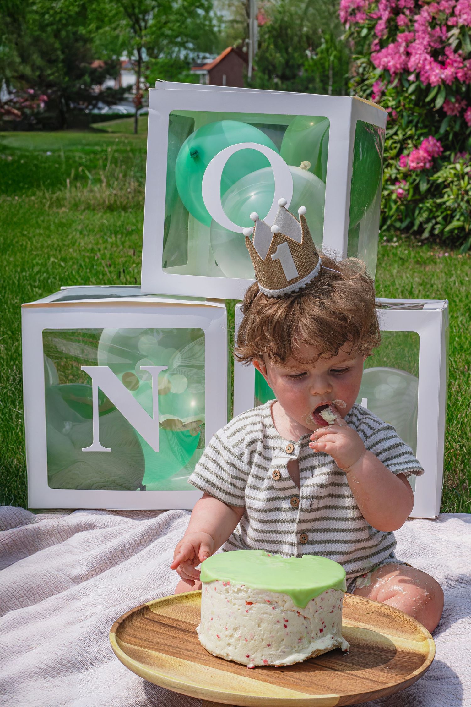 Baby zitten op kleed met een één jaar kroontje eten met zijn vinger van zijn taart tijdens een cakesmashshoot in Breda.