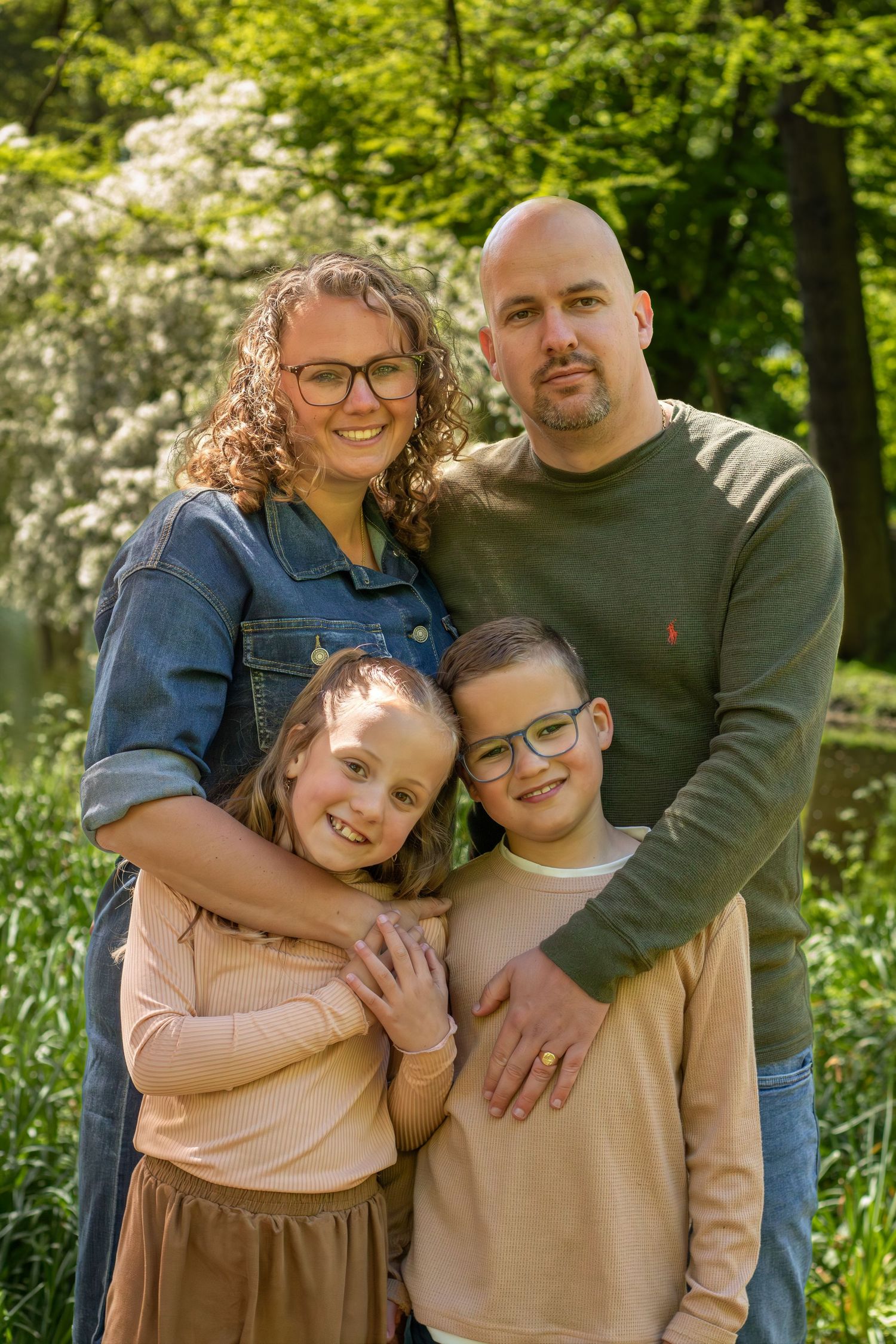 Een glimlachend gezin van vier poseert buiten in een weelderig groen park tijdens gezinshoot in Zuid-Holland.