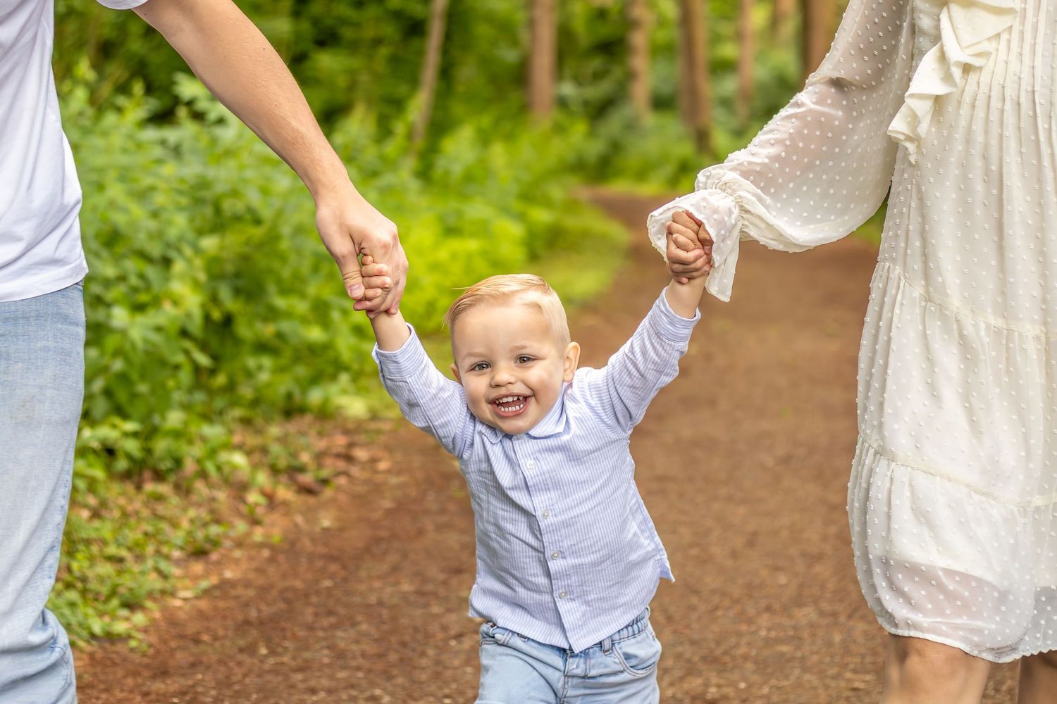 Jongetje vol plezier hand in hand lopend met papa en mama tijdens een gezinsshoot in Zuid-Holland.