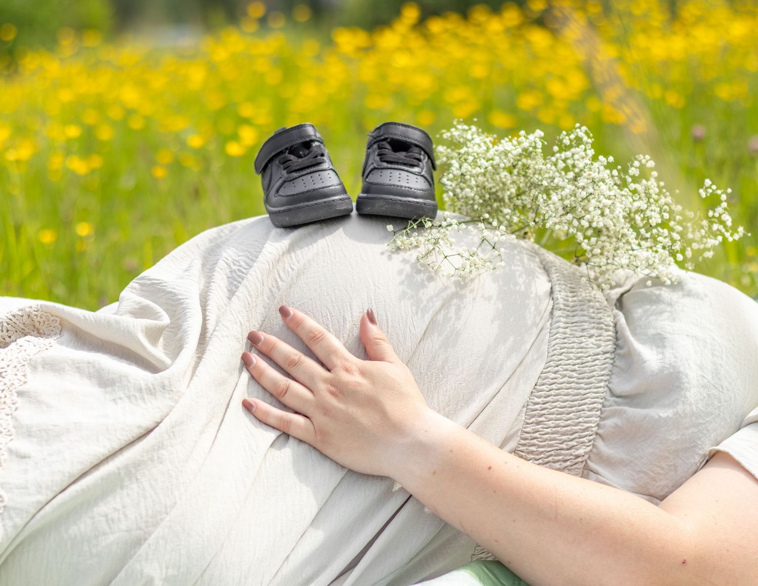 Zwangere vrouw in bloemenveld met kruid en babyschoentjes op buik tijdens een zwangerschapshoot in Zuid-Holland.
