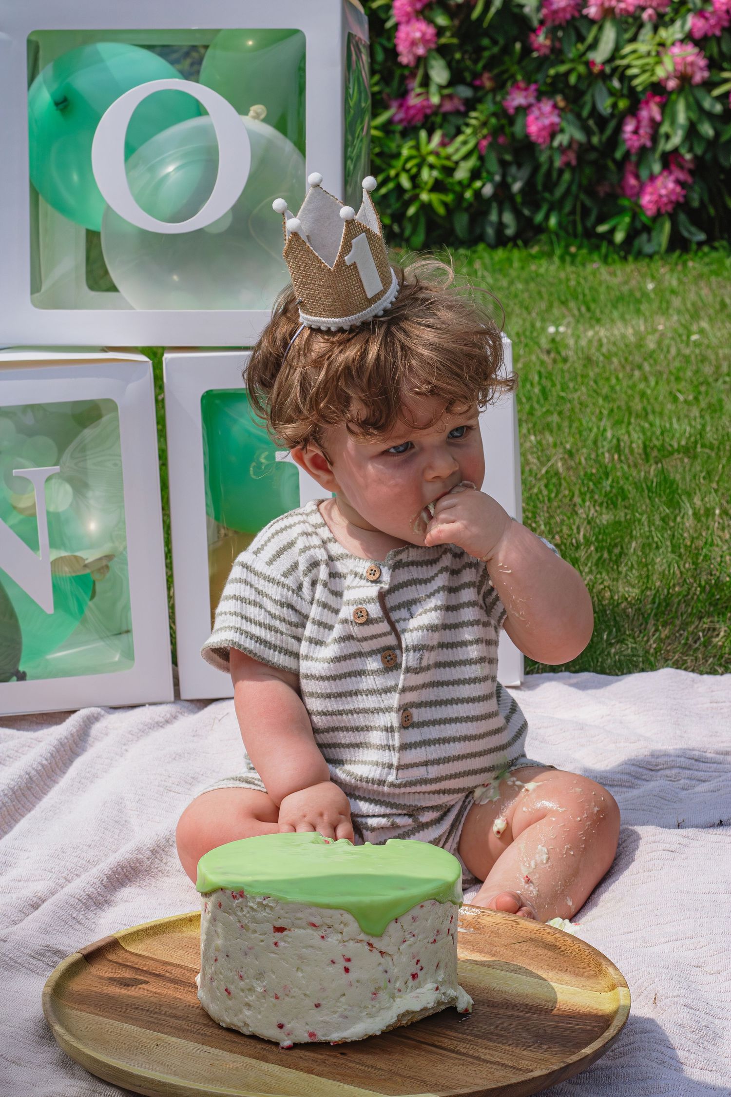 Baby zitten op kleed met een één jaar kroontje eten met zijn vinger van zijn taart tijdens een cakesmashshoot in Breda.