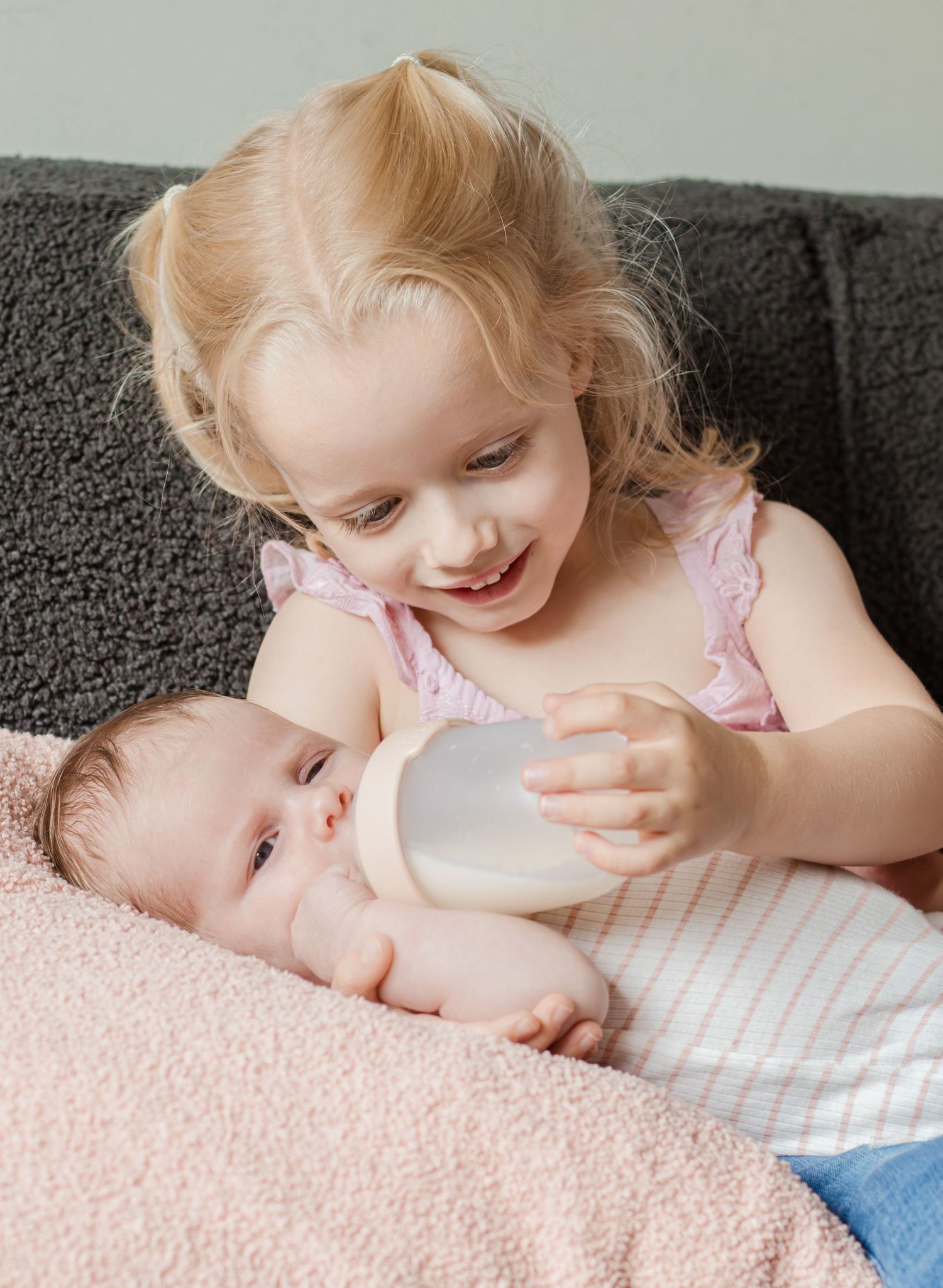 Grote zus die haar kleine zusje een flesje geeft tijdens een newbornshoot in Zuid-Holland.