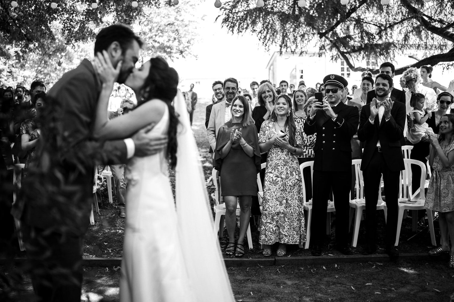 Couple s'embrassant en fin de cérémonie avec focus sur la foule qui les acclament, photo en noir et blanc