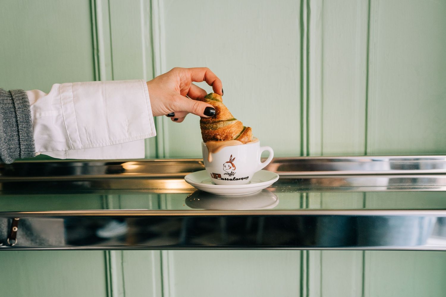 woman dipping a pistachio croissant into a Italian coffee in a cafe in Stockholm, Sweden