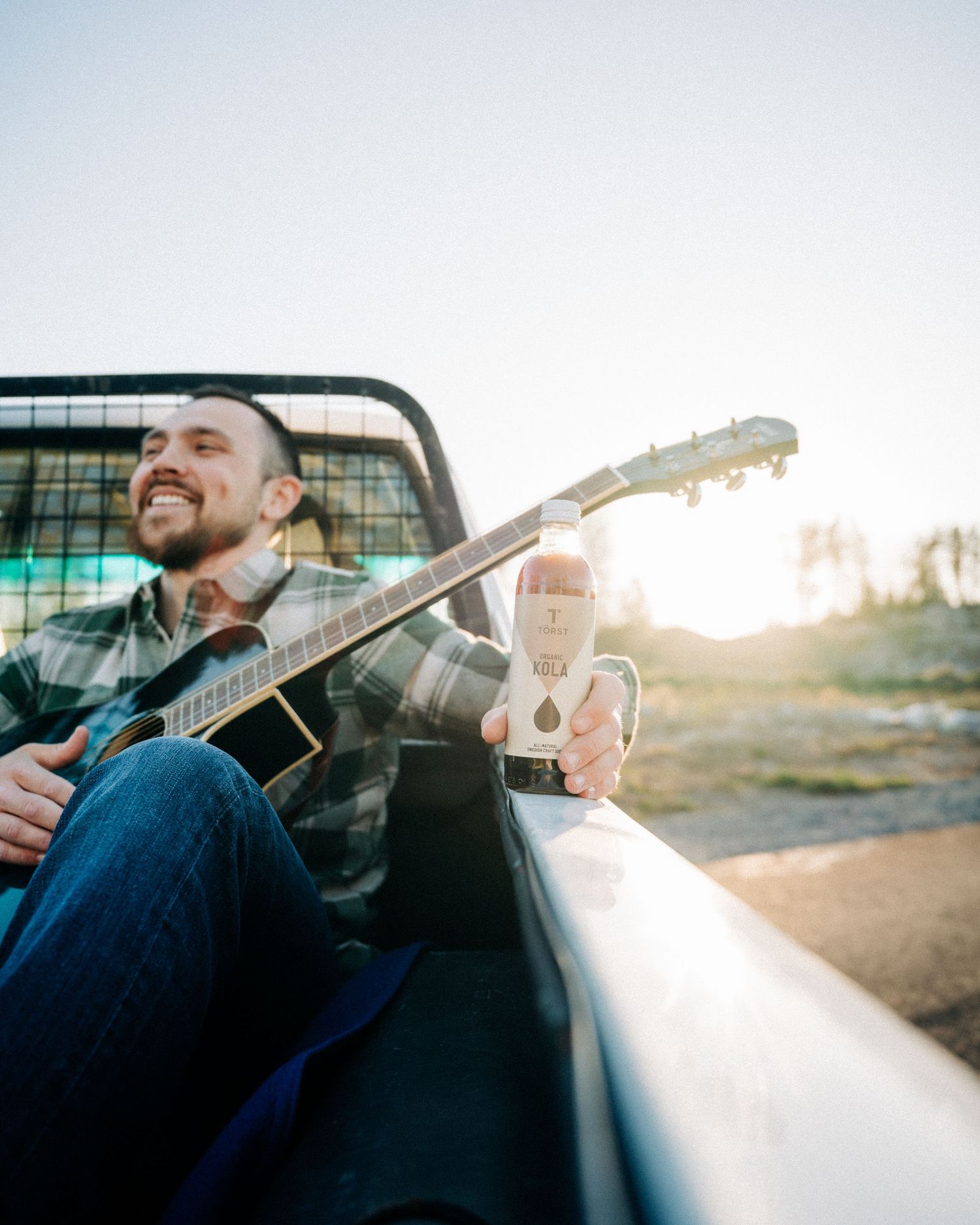 man playing the guitar in the back of a pick up truck drinking Törst kola flavoured organic drink