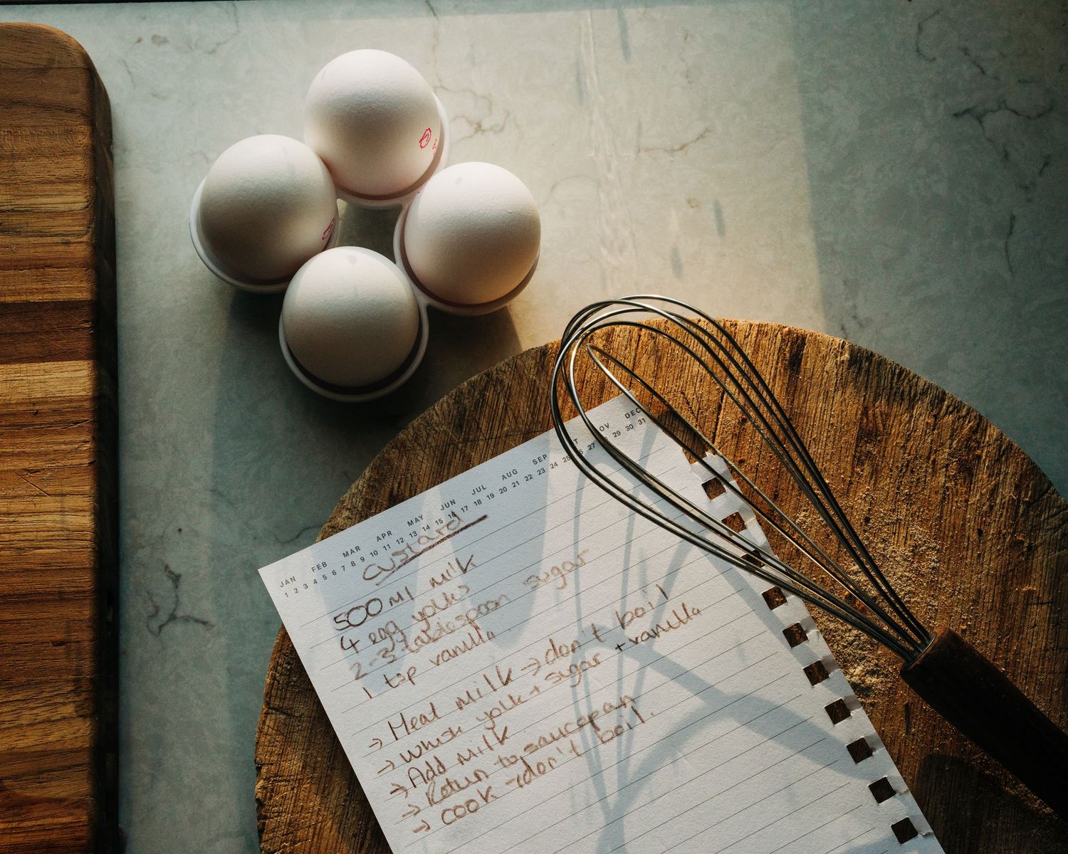 homemade custard recipe written on paper with ingredients on a home kitchen table photographed for a commercial cook book photoshoot.