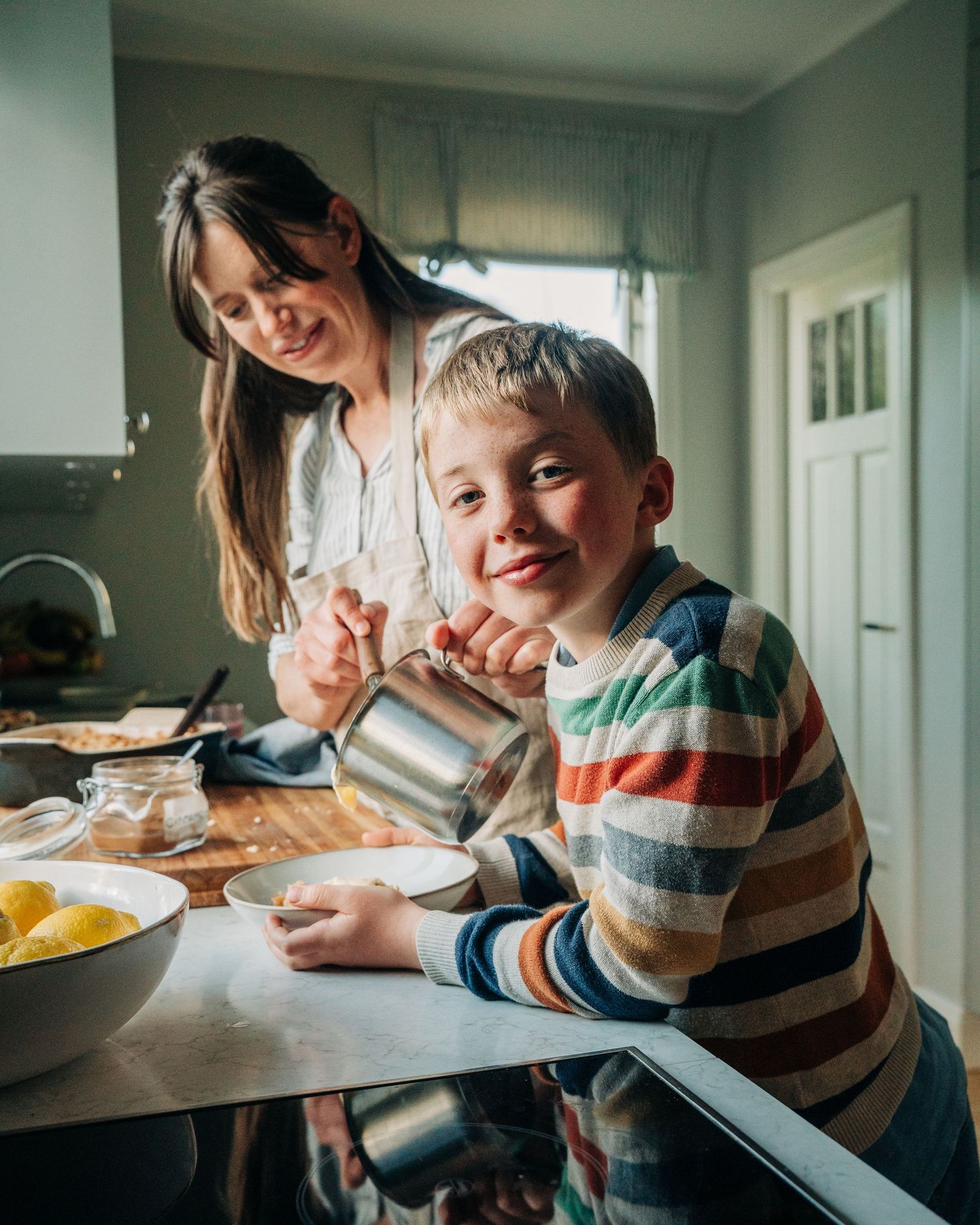 child looking at the camera whilst his mum plates his food. Lifestyle commercial food photography shoot in Stockholm, Sweden