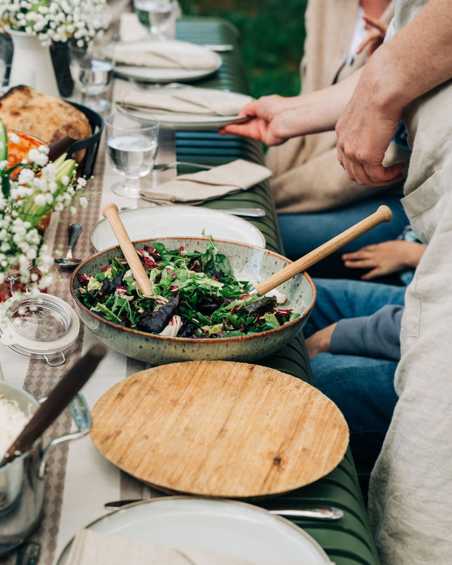 woman serving salad on a decorated table in the garden for a commercial food photography shoot in Stockholm, Sweden.