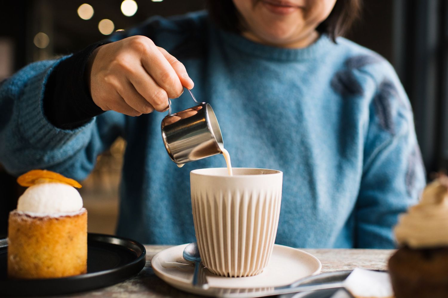 Woman pouring milk into a cup of coffee in a cafe for commercial lifestyle photography food and beverage
